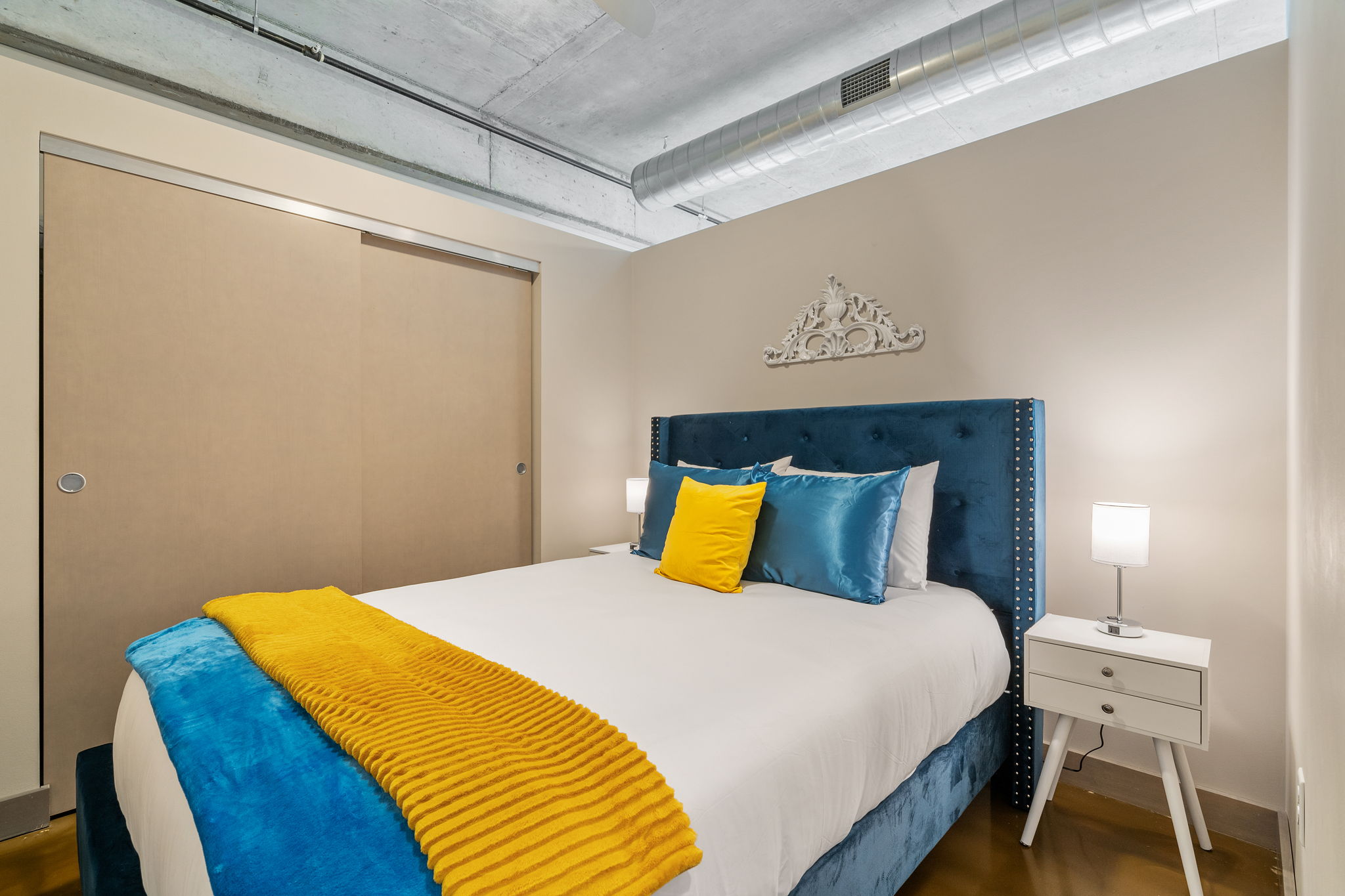 A stylish modern bedroom featuring a cozy blue bed and bright yellow accents.