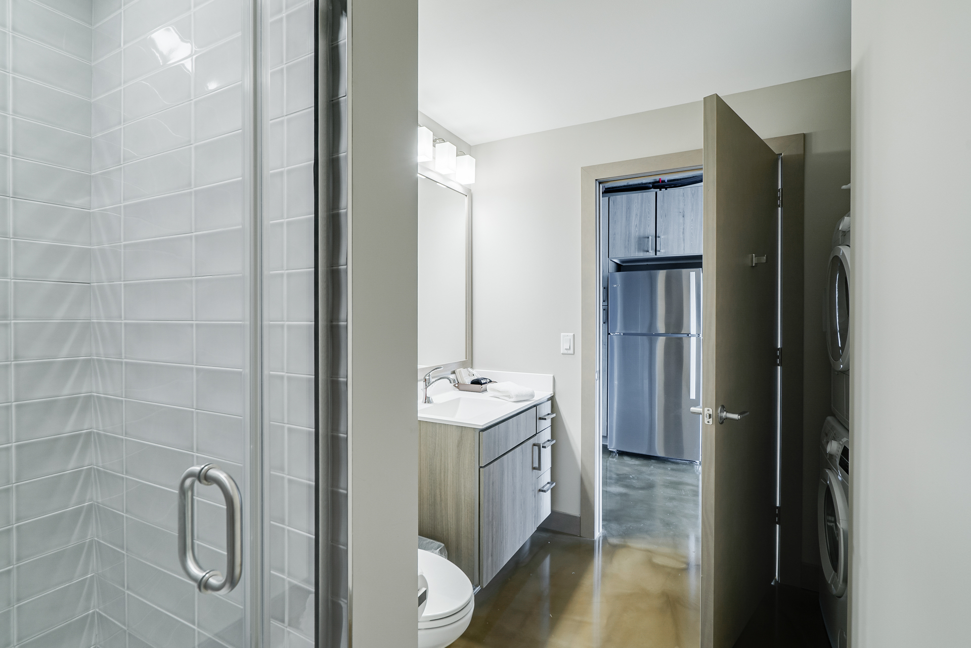 A sleek modern bathroom leading into a compact kitchen area.
