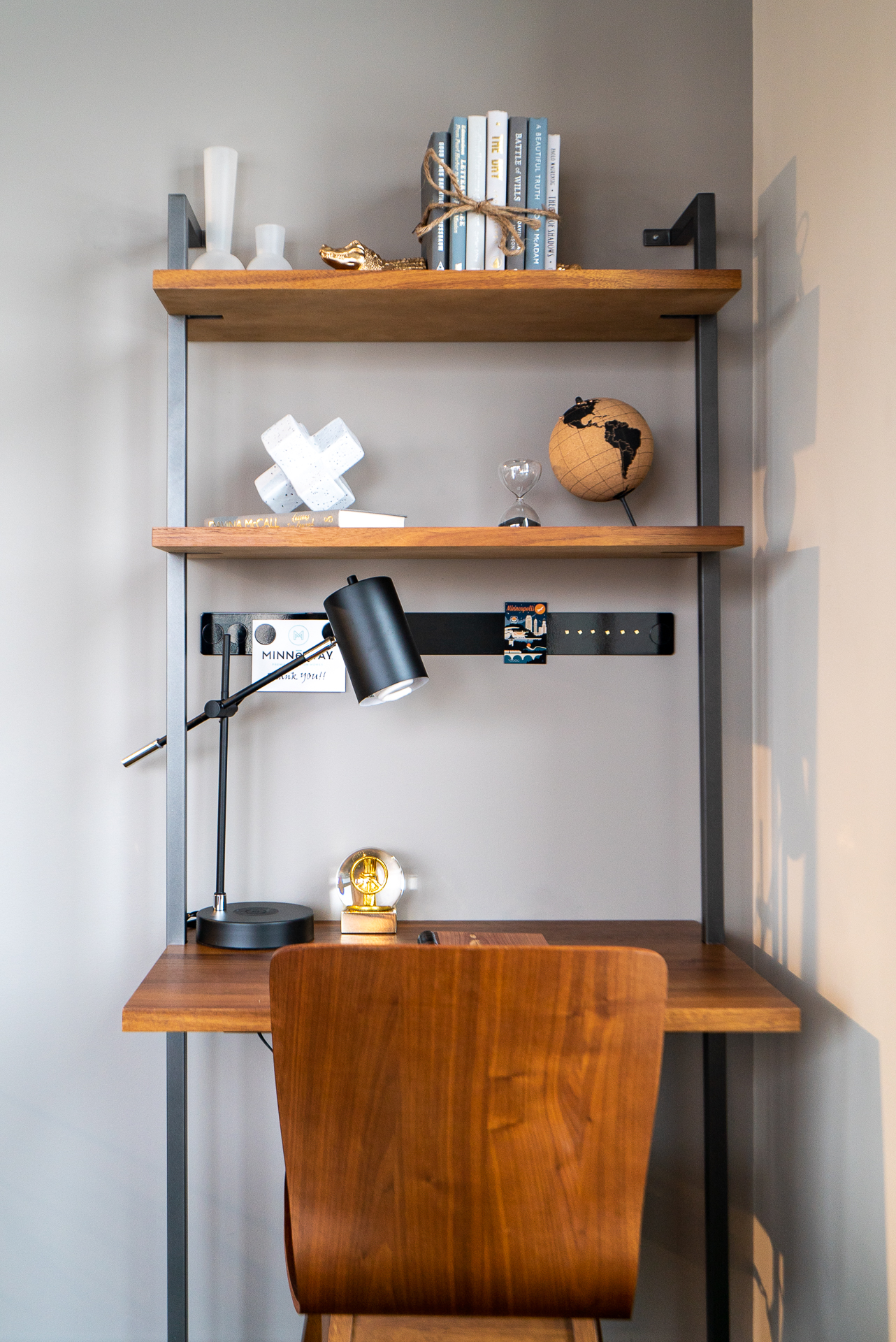 A modern workspace featuring a wooden desk, decorative shelves, and a stylish desk lamp.