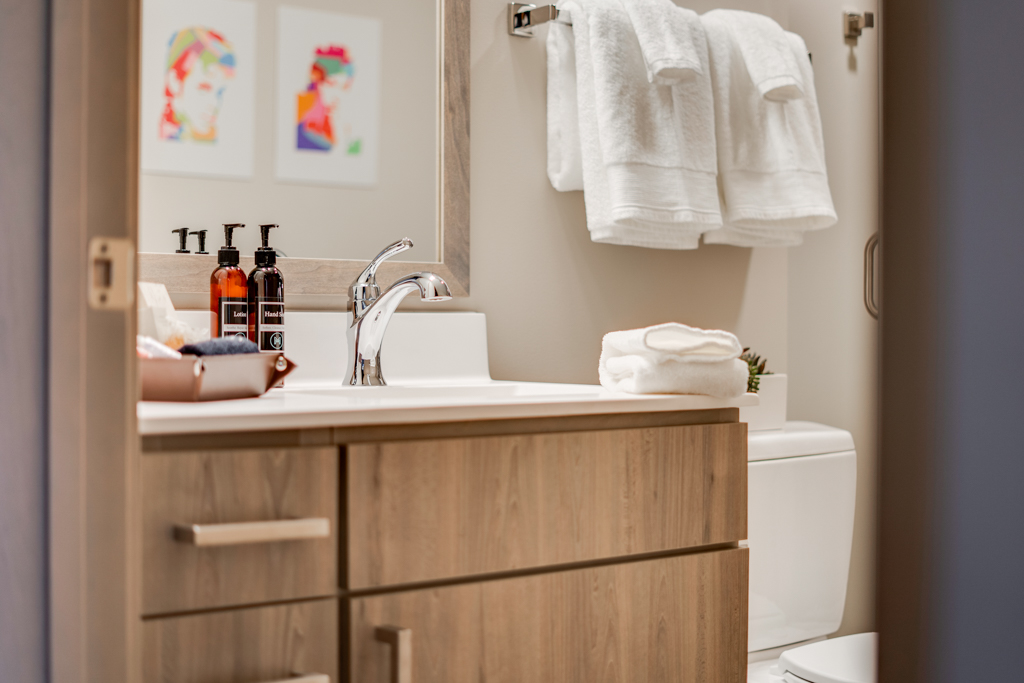 A stylish and modern bathroom with a minimalist design, featuring a clean sink area, fluffy towels, and colorful artwork.