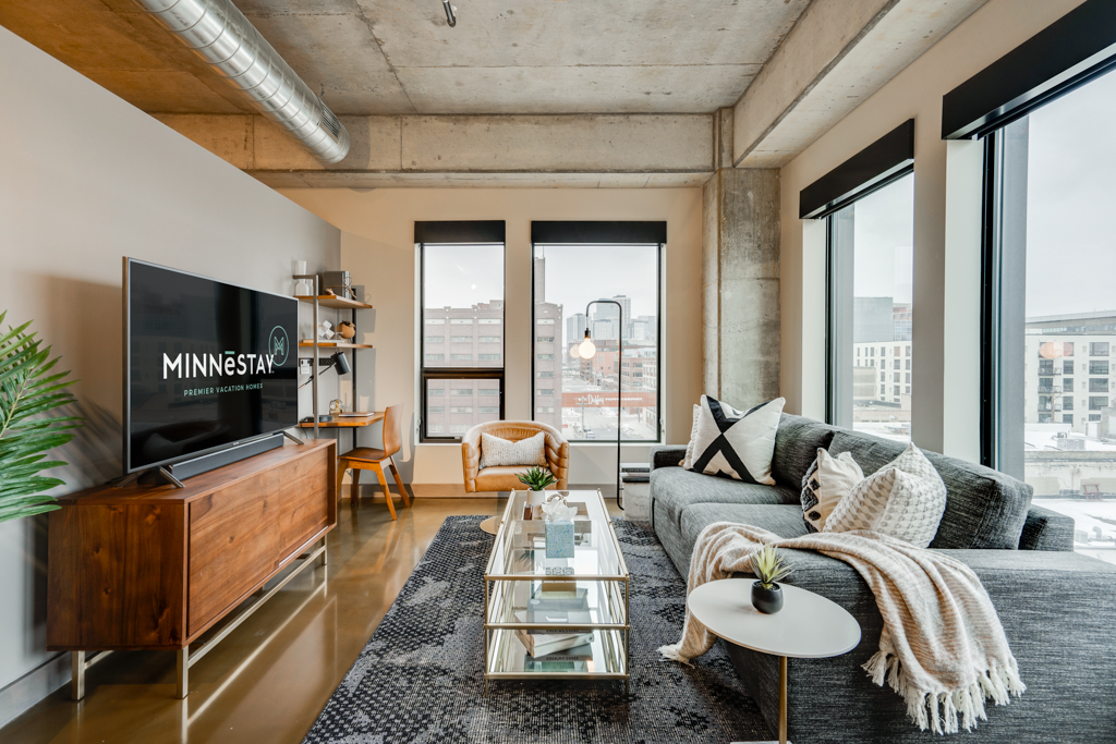 Modern living room with a sectional sofa, coffee table, and large windows showcasing an urban view.