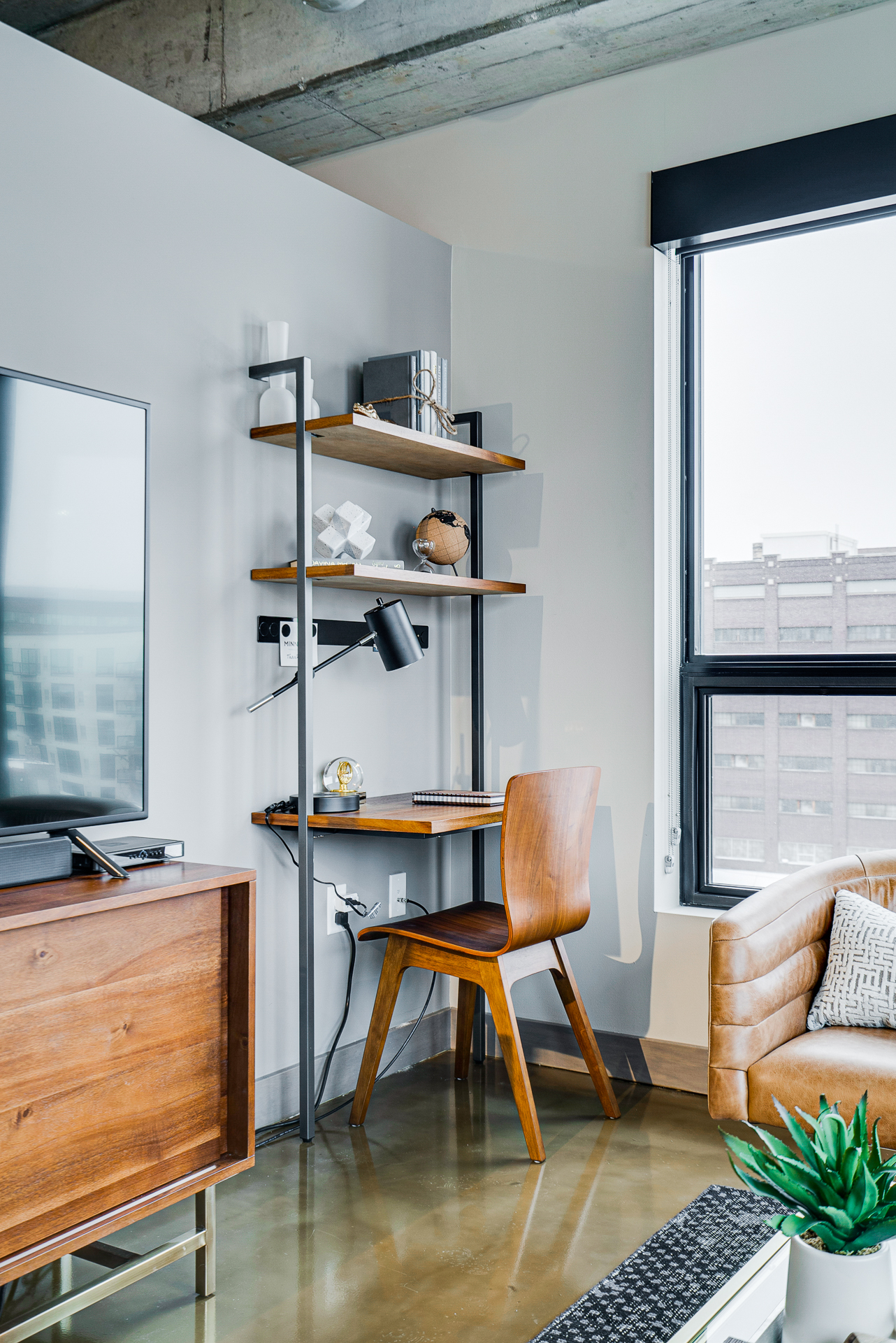 A modern home office featuring a wooden desk, stylish shelving, and a cozy leather sofa.