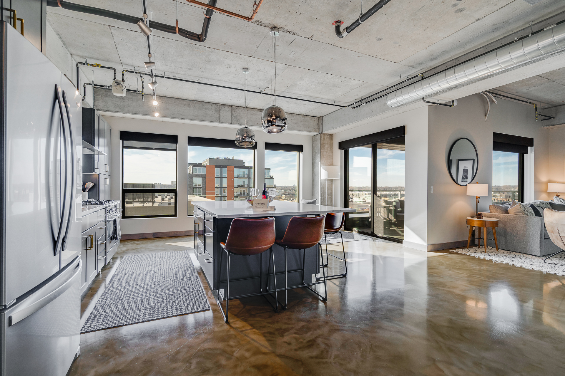 Modern kitchen and living space featuring an island, bar stools, and large windows.