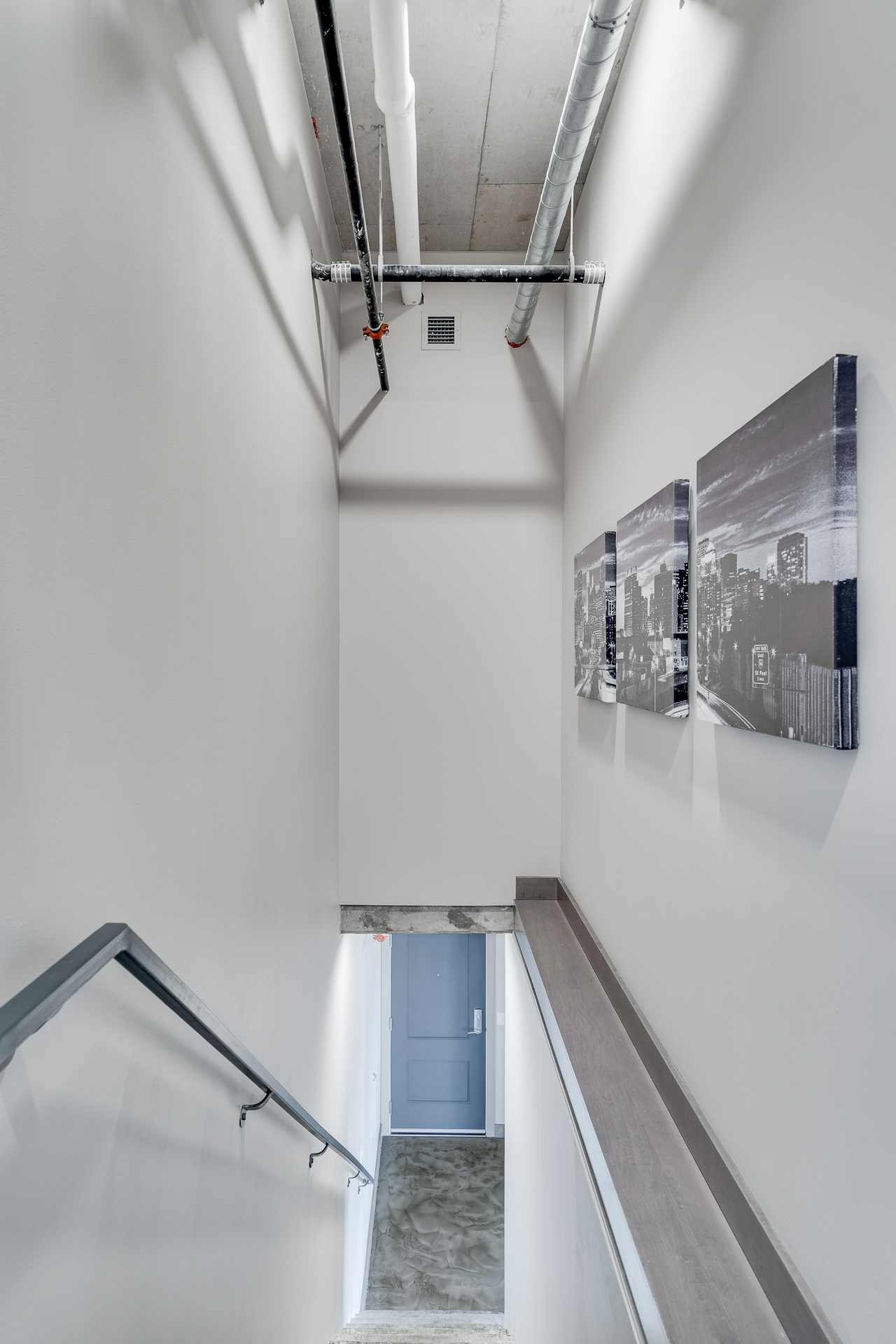 A modern staircase leading to a grey door, decorated with cityscape artworks.