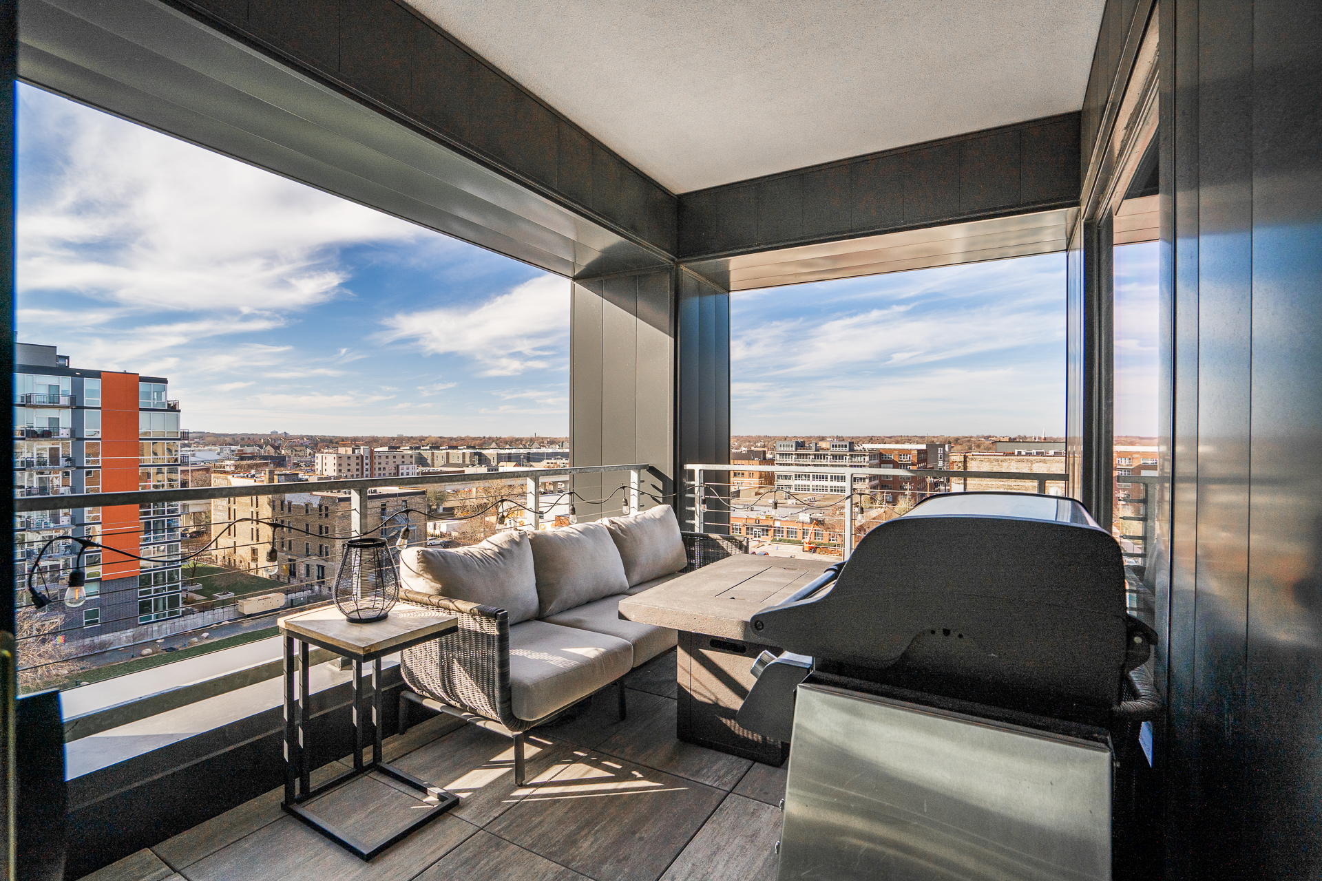 A modern balcony offering stunning city views with stylish seating and a grill.