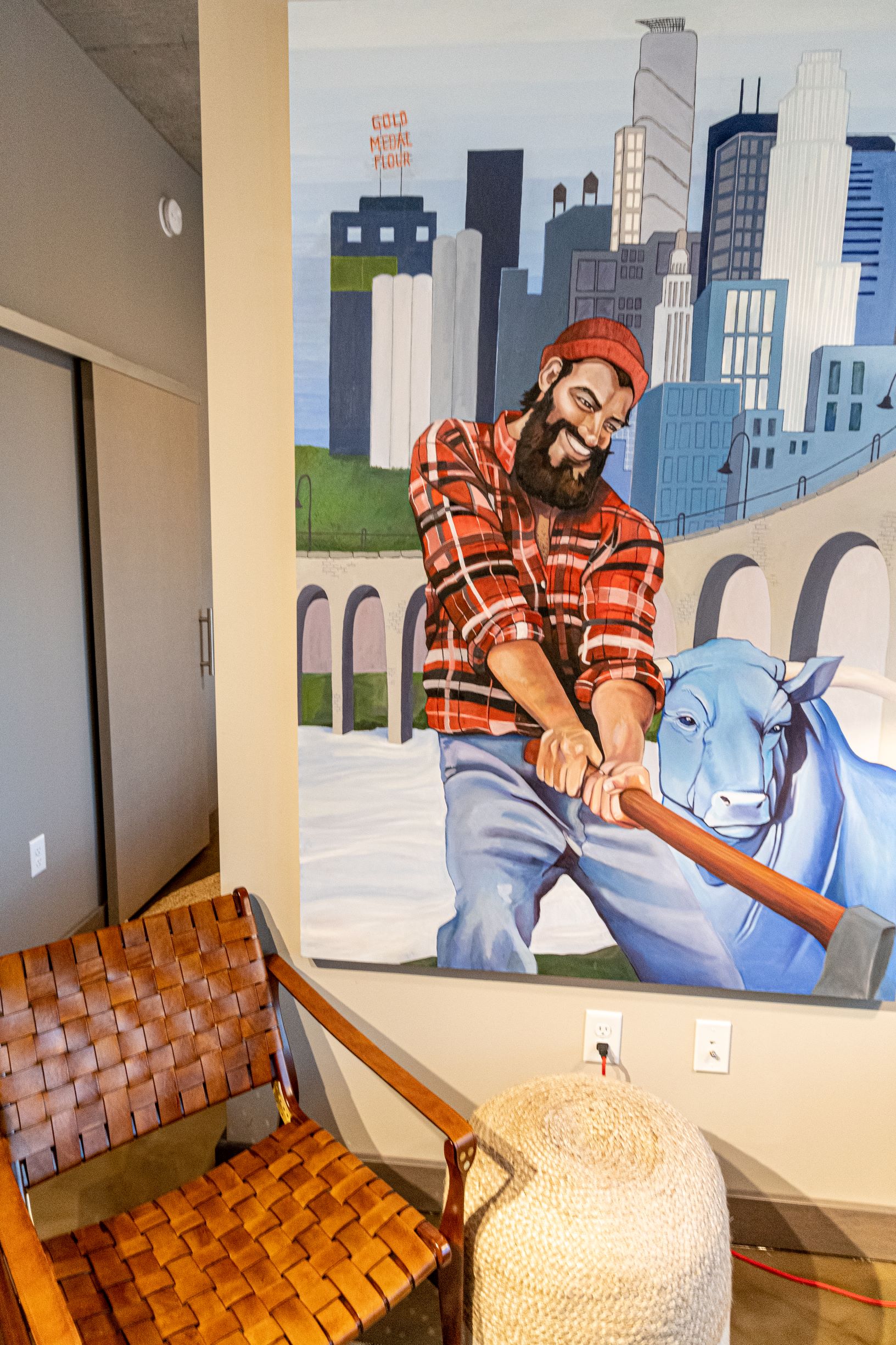 A colorful mural featuring a smiling man in a plaid shirt and a blue cow, set against a city skyline.