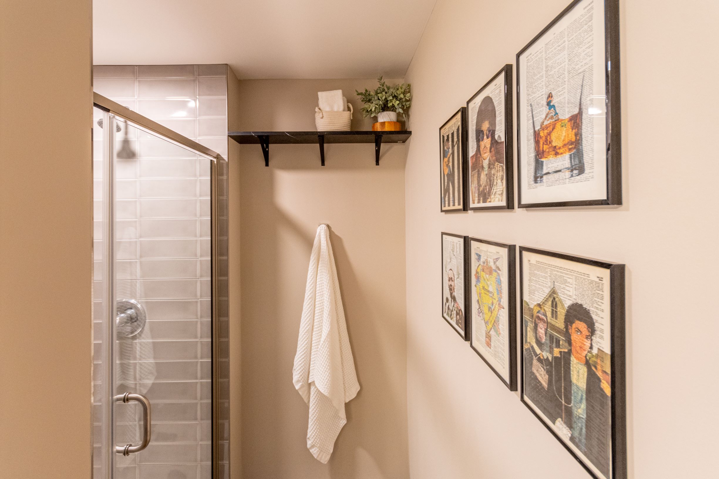 A stylish bathroom corner featuring a glass shower, towel rack, shelf with decor, and framed art.