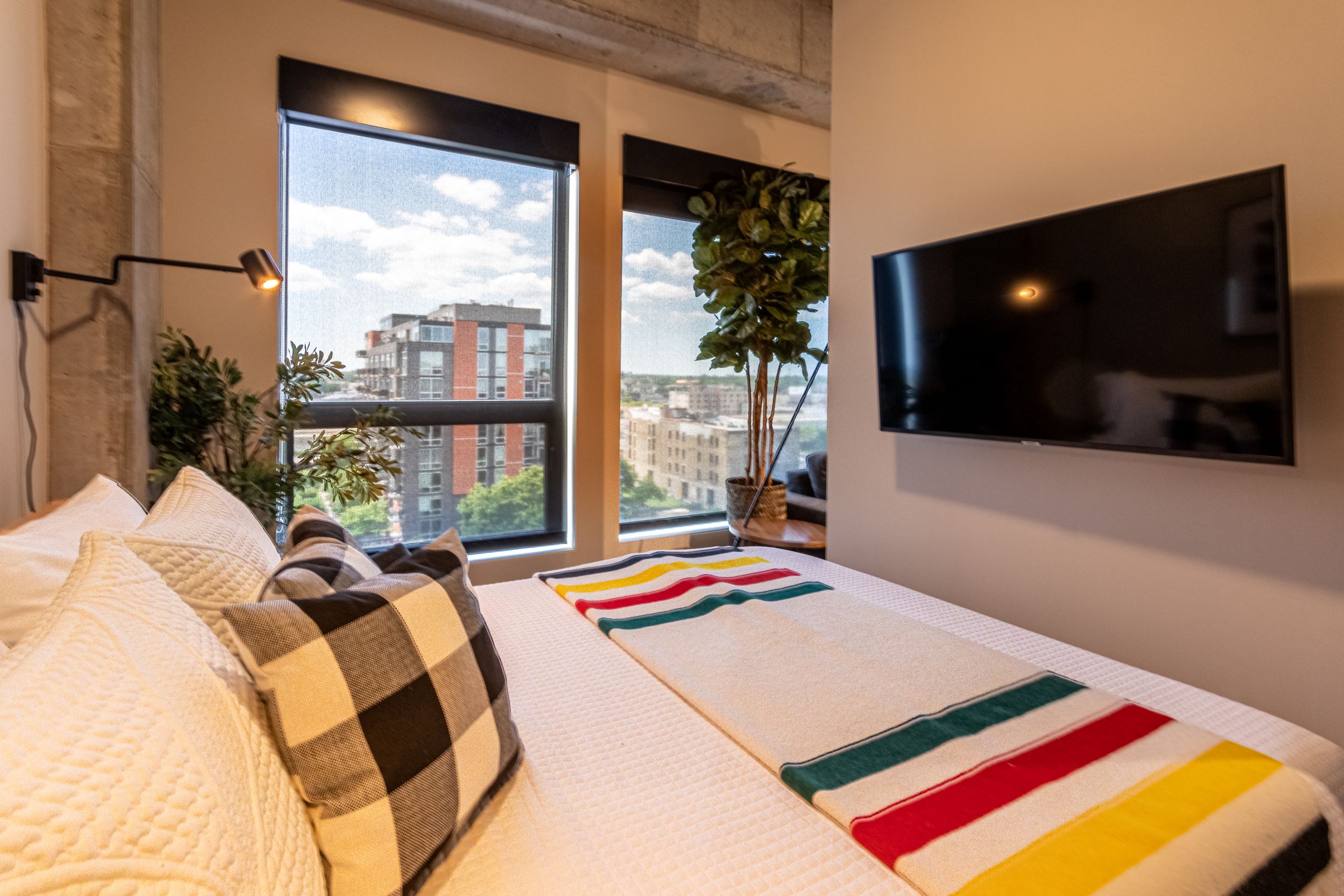 A cozy modern bedroom with a view, featuring a neatly made bed and decorative pillows.