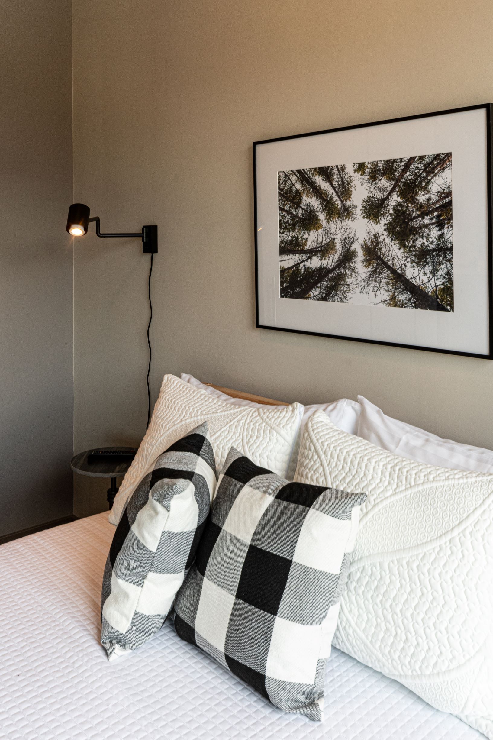 A modern bedroom corner with a cozy bed, decorative pillows, and artistic wall decor.