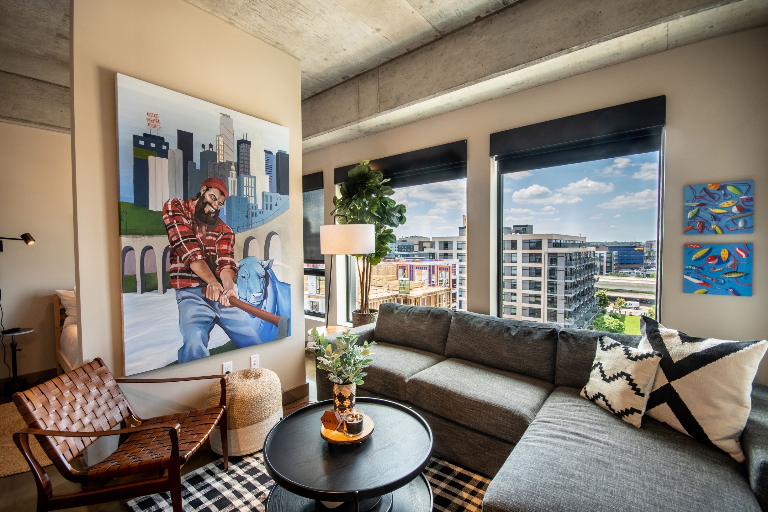A stylish interior featuring a vibrant mural, a comfortable grey couch, and large windows overlooking a cityscape.
