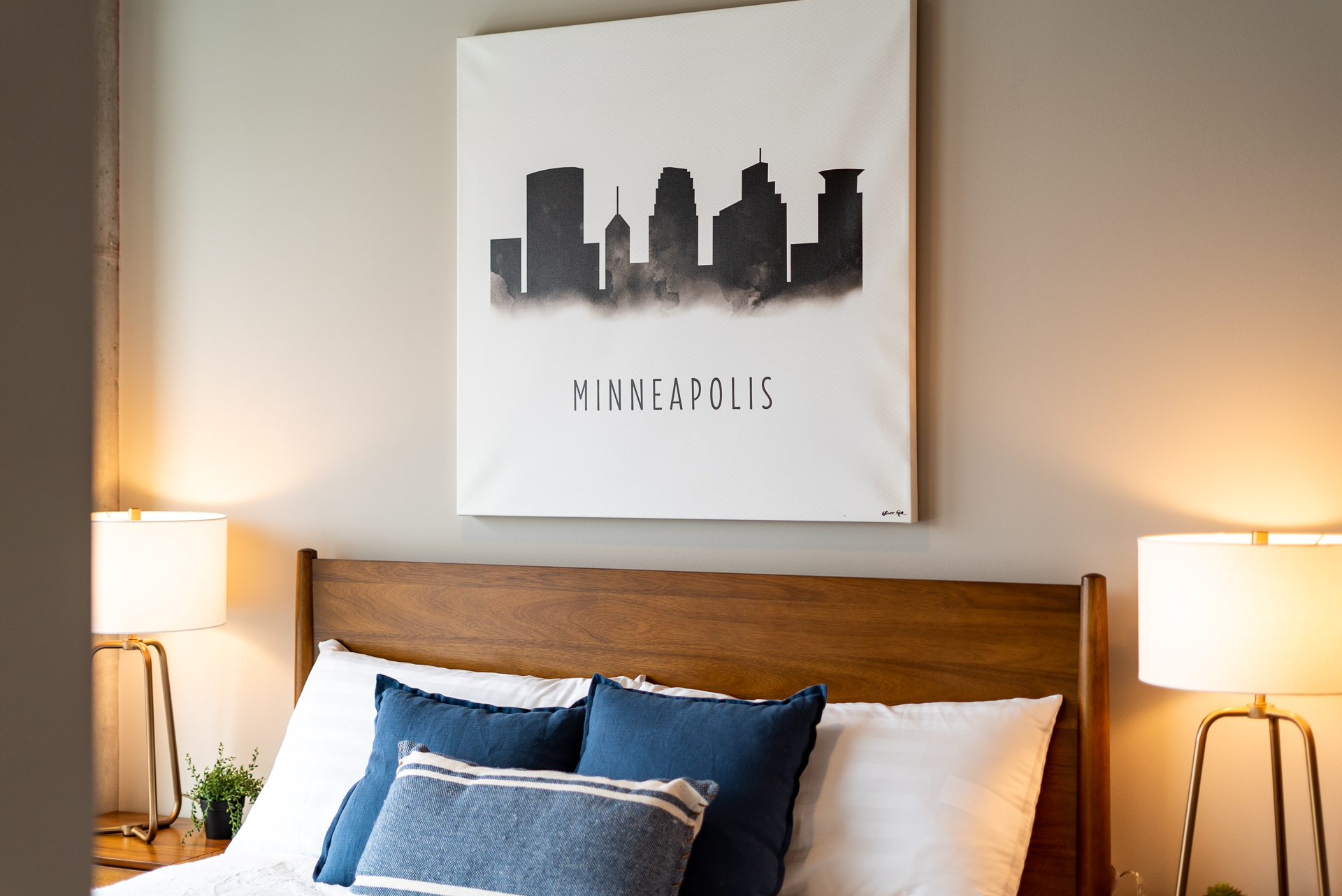 A cozy bedroom featuring a Minneapolis skyline canvas above a wooden bed.