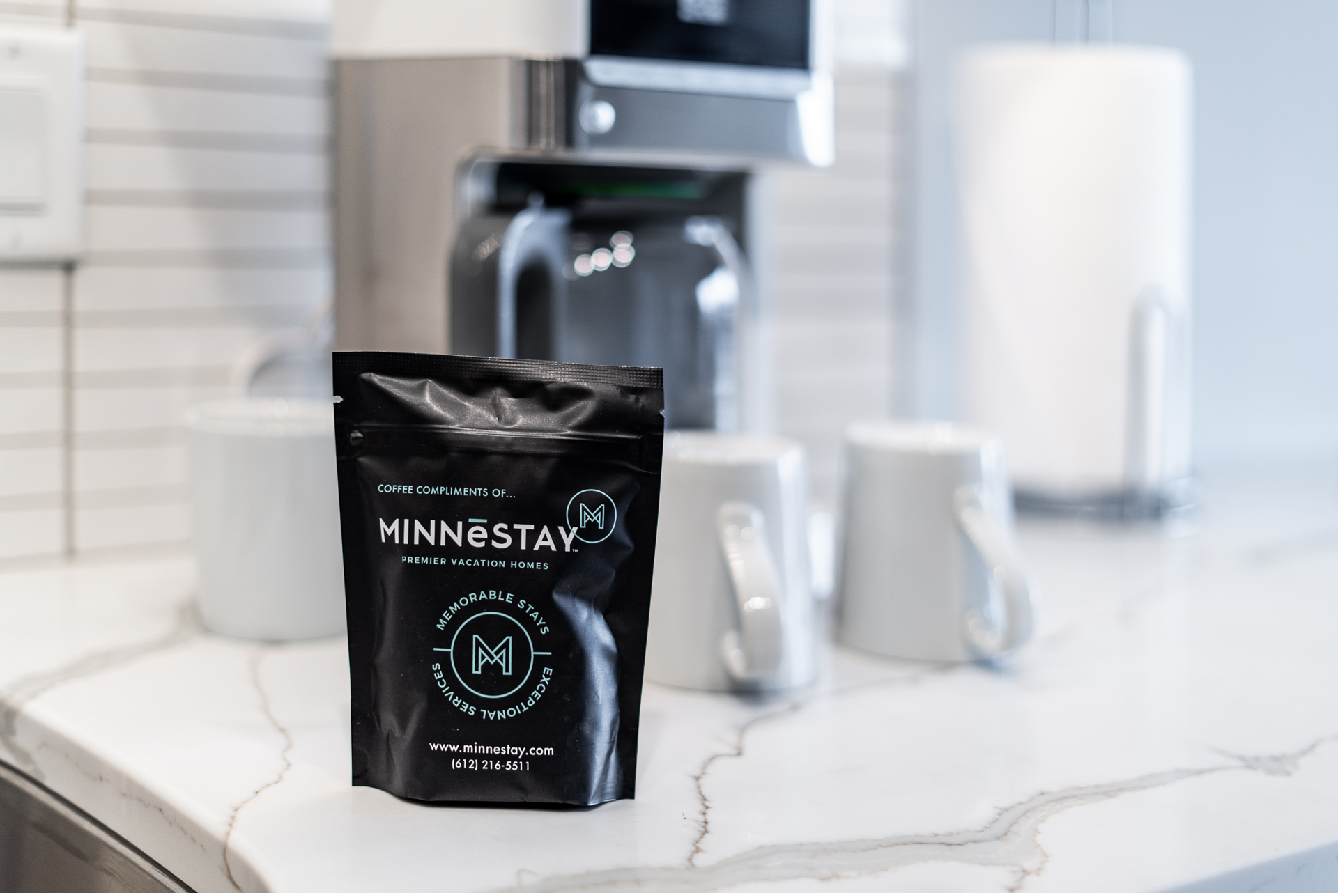 A stylish coffee bag from Minnēstay placed elegantly on a marble countertop alongside white coffee mugs.