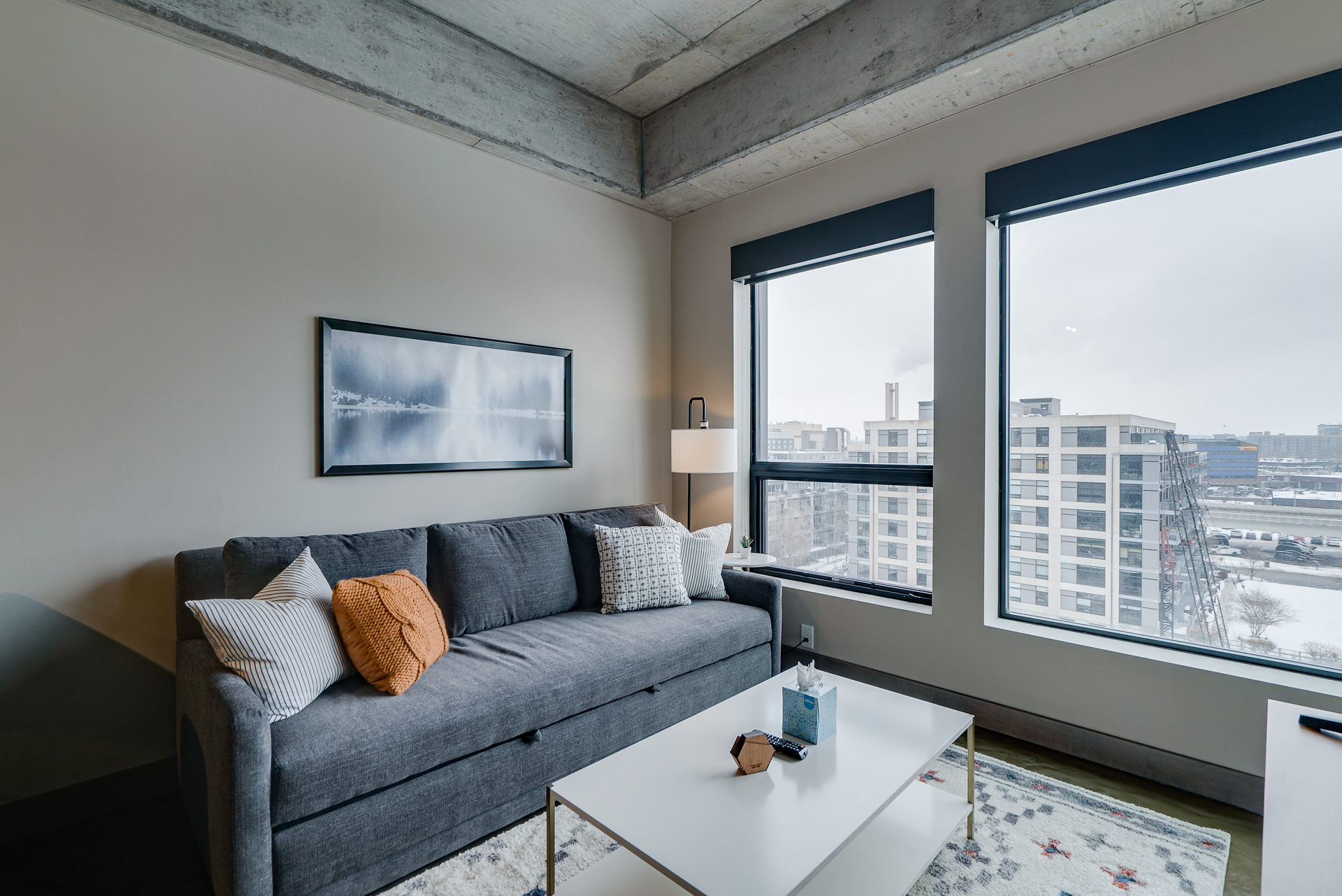 A modern living room with gray sofa and contemporary decor, featuring large windows with urban views.