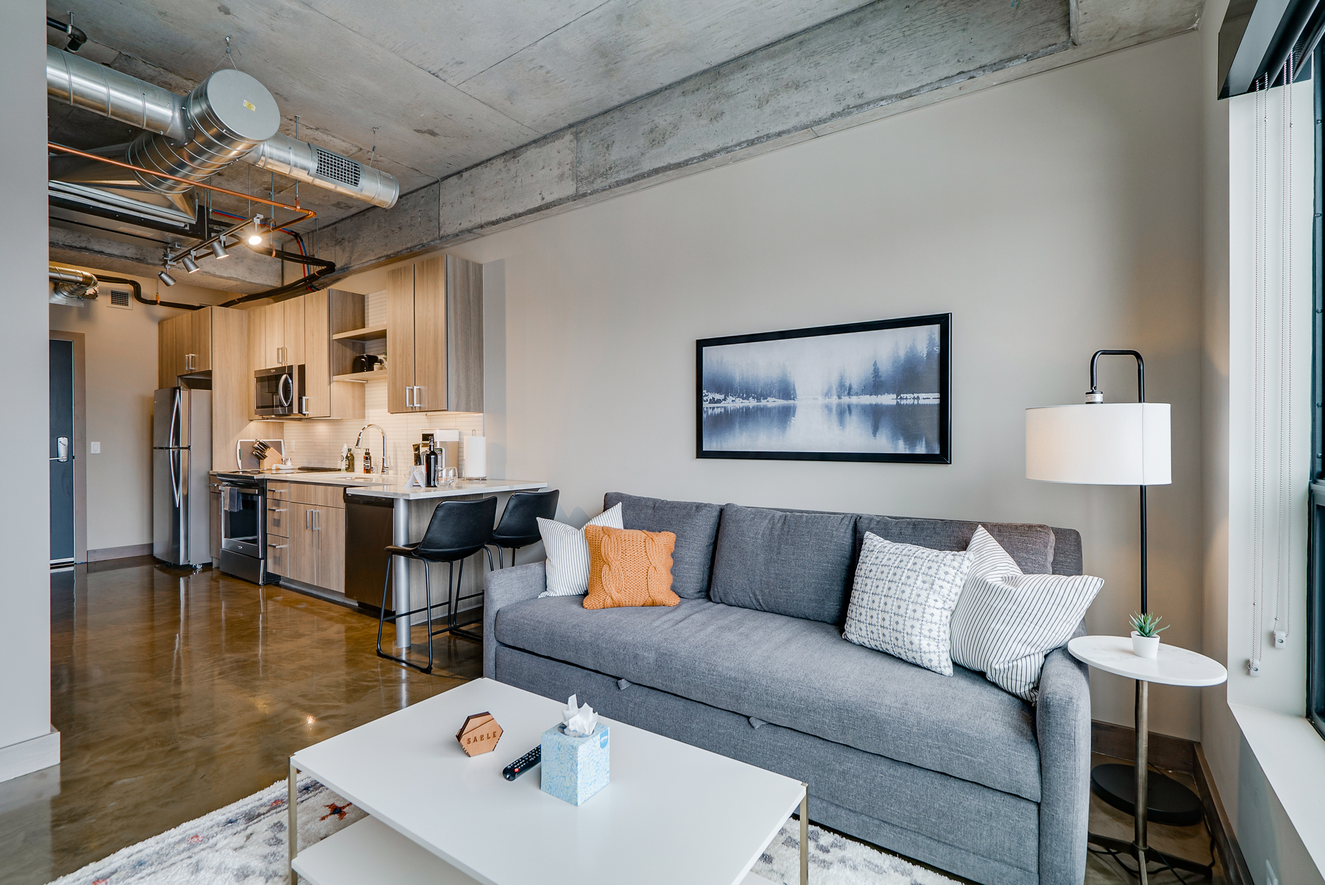 A stylish apartment living room with a gray couch, a small coffee table, and an open kitchen area.