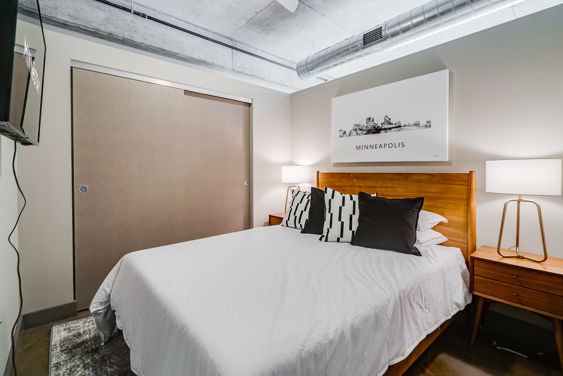 A modern and minimalist bedroom featuring a wooden bed, stylish pillows, and a skyline artwork.