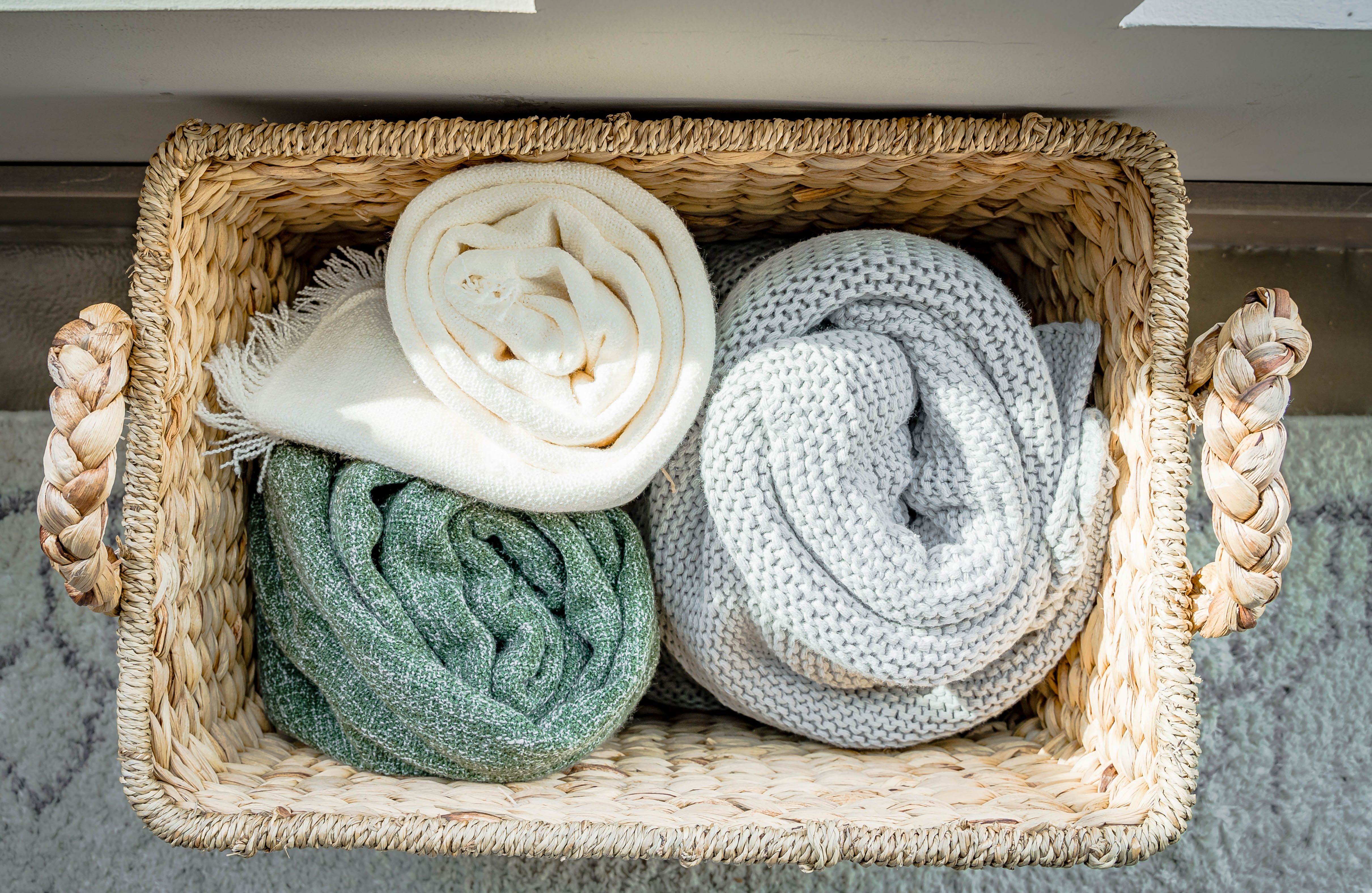 A woven basket filled with cozy rolled blankets in soft colors.