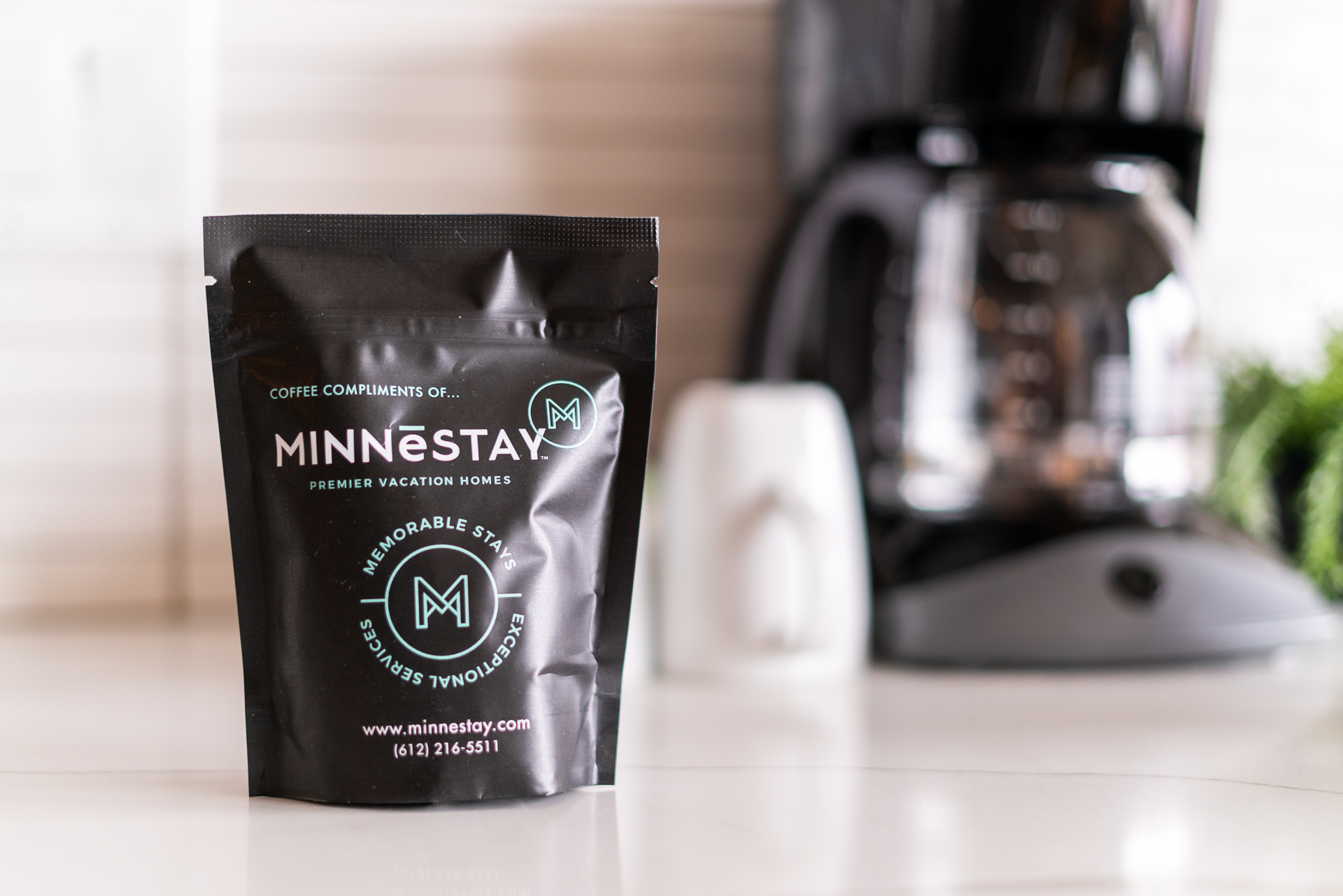 A stylish coffee package from MINNESTAY set against a blurred coffee maker.