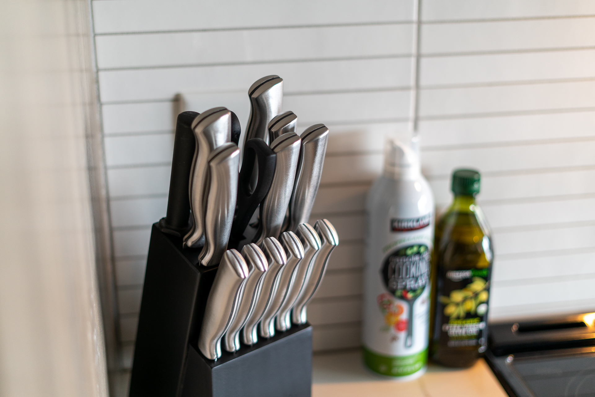 A stylish knife block with modern kitchen knives beside cooking oil and spray.