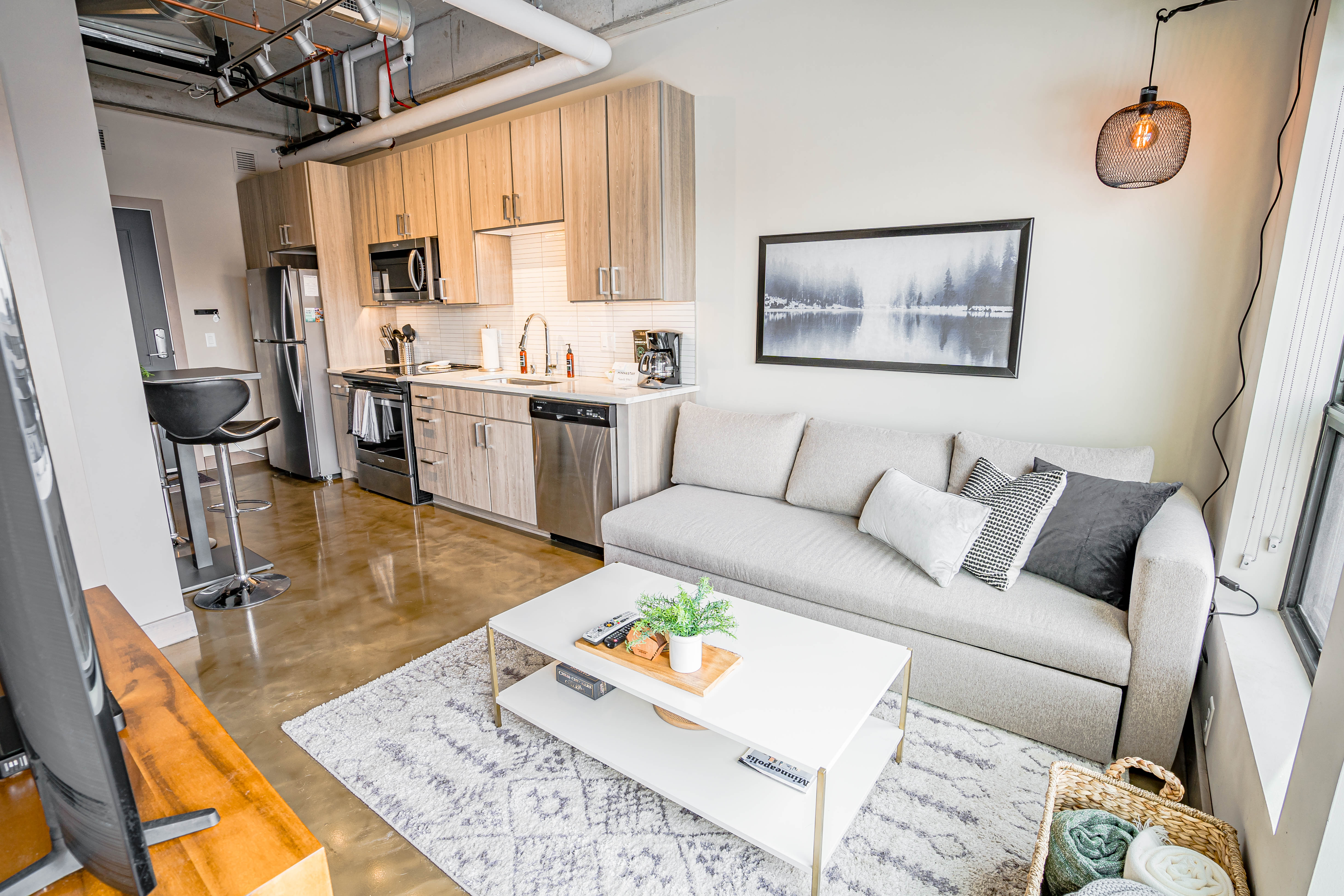 Stylish living space featuring a kitchen and a cozy gray sofa with decorative cushions.