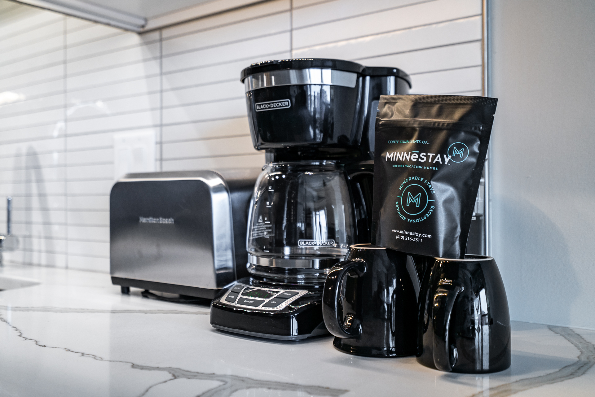 A stylish coffee setup featuring a Black & Decker coffee maker, MINNESTAY coffee, and matching mugs.