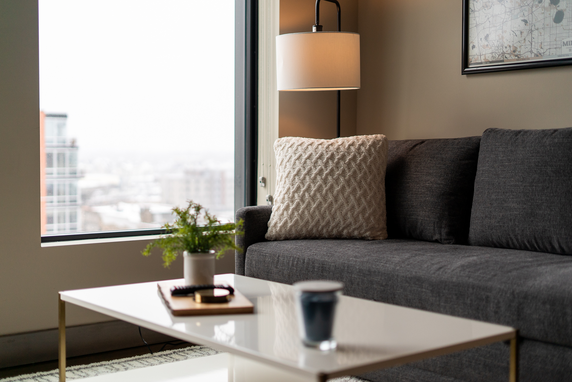 A cozy living room corner featuring a dark gray sofa and a bright view of an urban landscape.