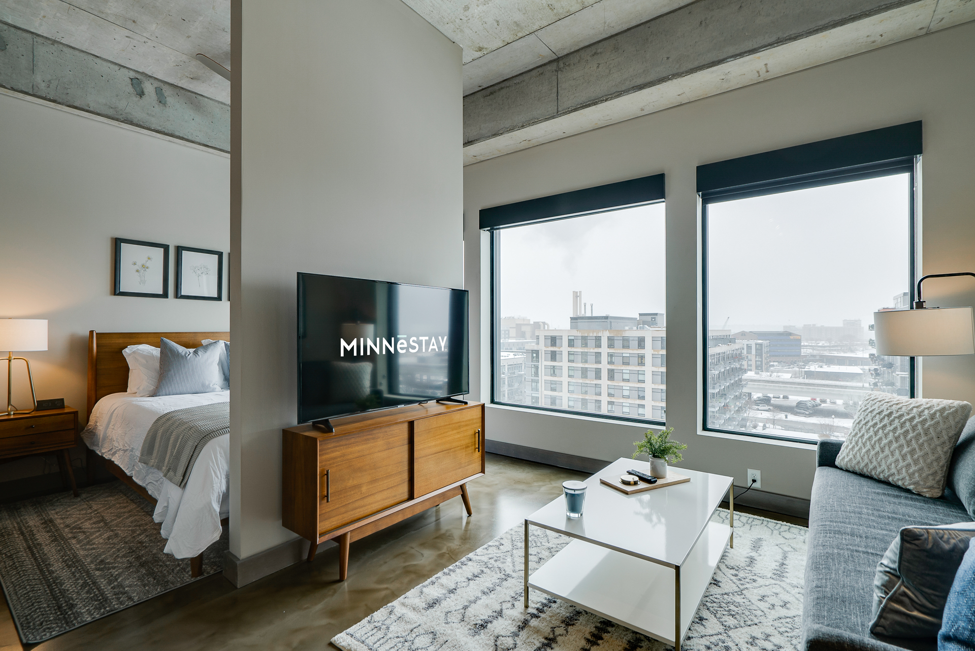 A modern living area with a cozy bedroom and stylish decor, featuring large windows and inner-city views.