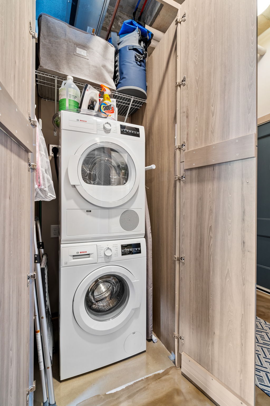 An organized laundry nook featuring a stacked washer and dryer with cleaning supplies above.