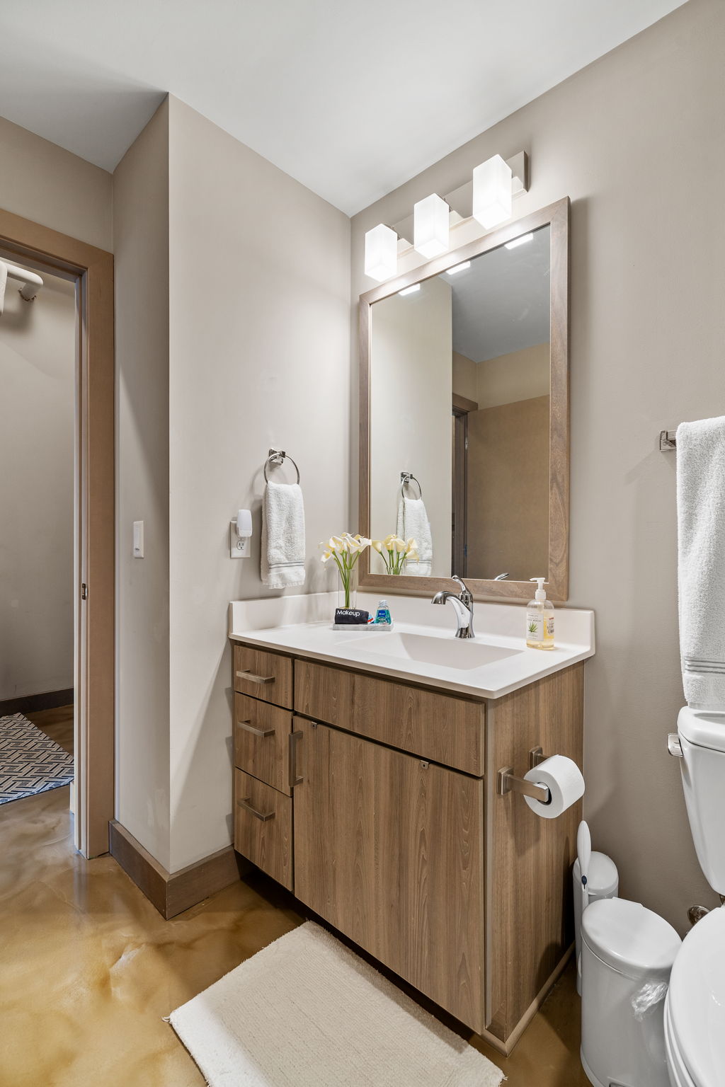 A modern and stylish bathroom featuring a wooden vanity and polished concrete floor.