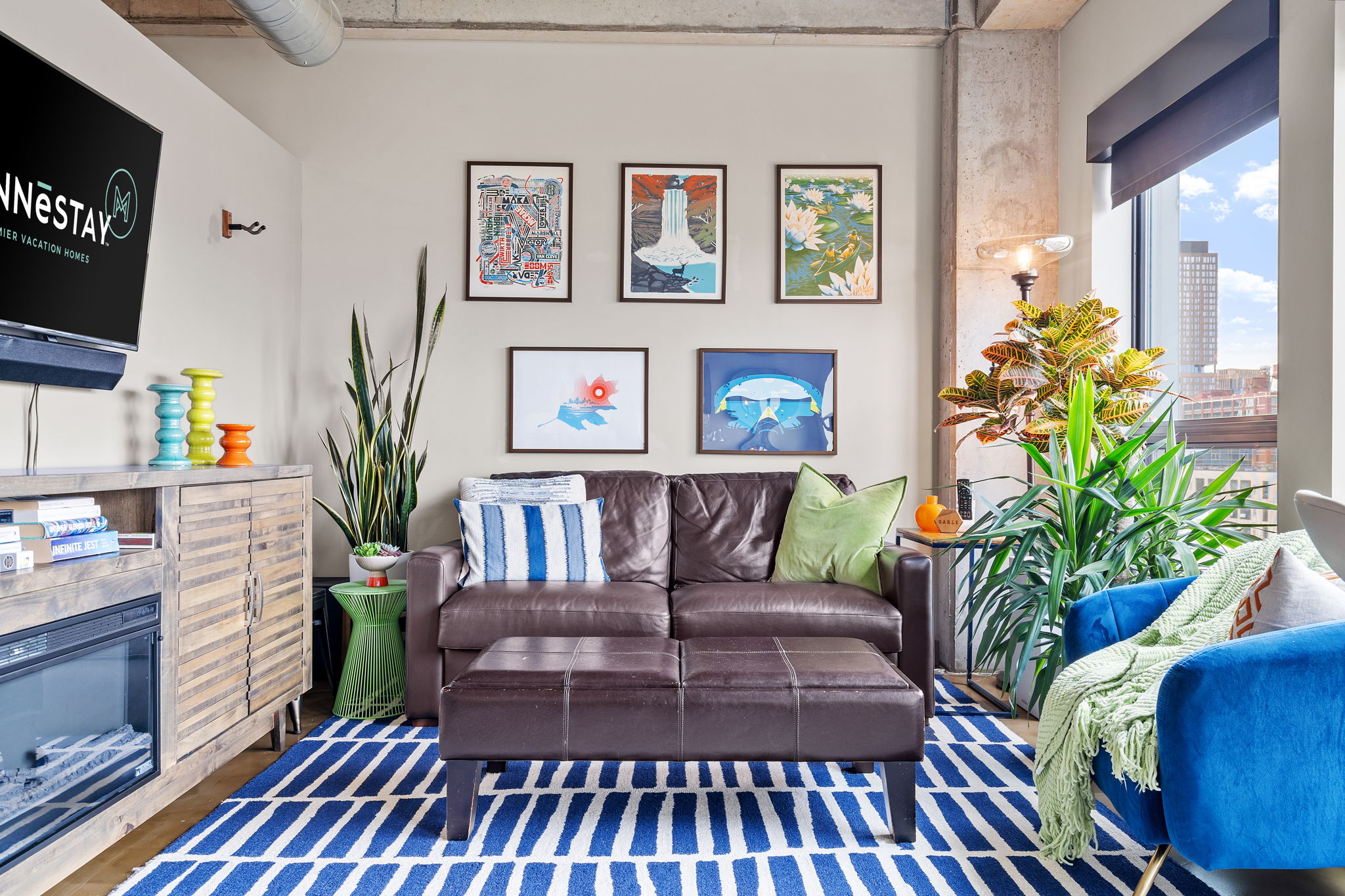 Cozy living room featuring a brown leather sofa, colorful artwork, and indoor plants.
