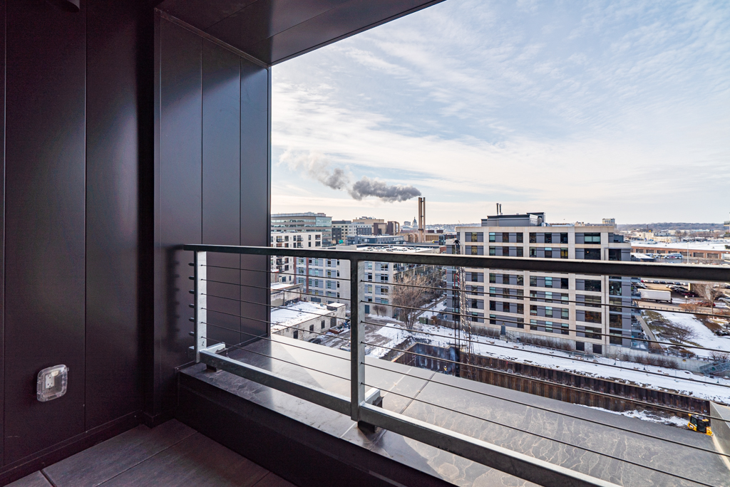 A modern balcony view of an urban landscape with smoke rising in the distance.
