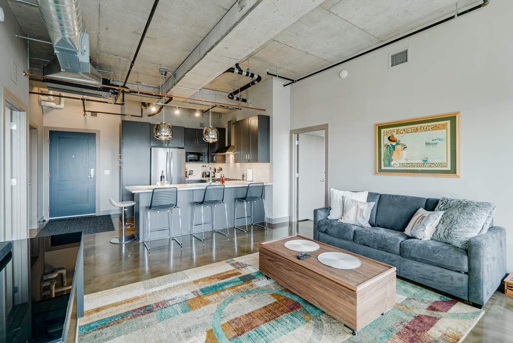 Stylish open-concept living space featuring a kitchen and living area with gray couch and dark cabinetry.