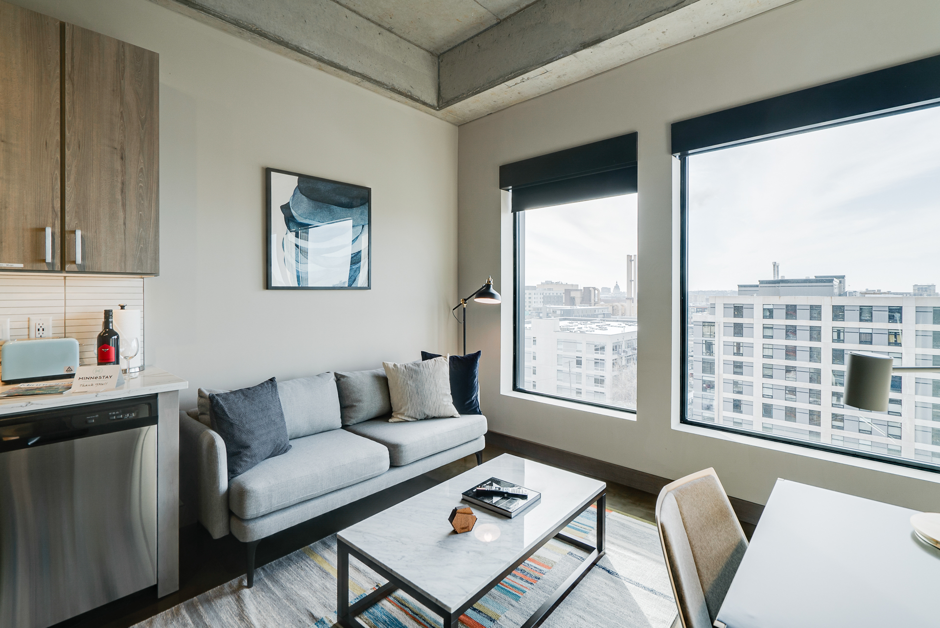 A modern and stylish living area featuring a gray couch and large windows with city views.