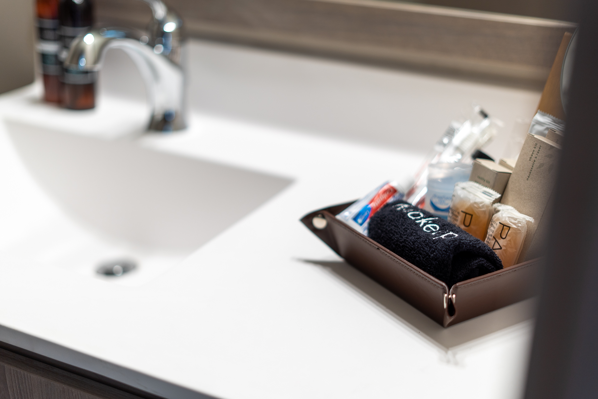 A modern bathroom countertop featuring a leather organizer filled with personal care items and a sleek chrome faucet.