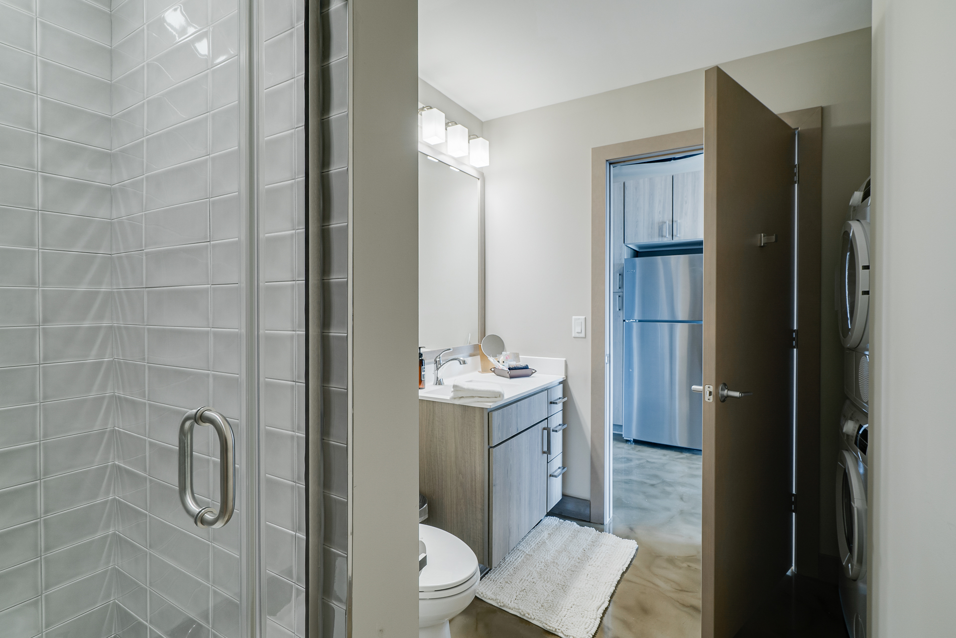 A modern bathroom with a sleek shower and vanity, leading to a kitchen area.
