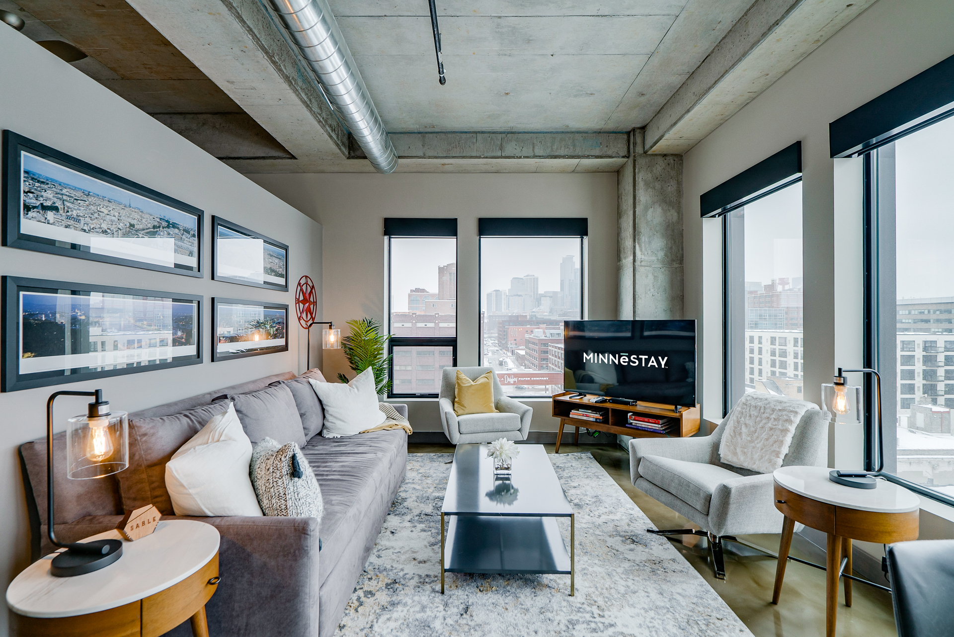 A contemporary living room featuring a grey sofa, large windows with city views, and stylish decor elements.