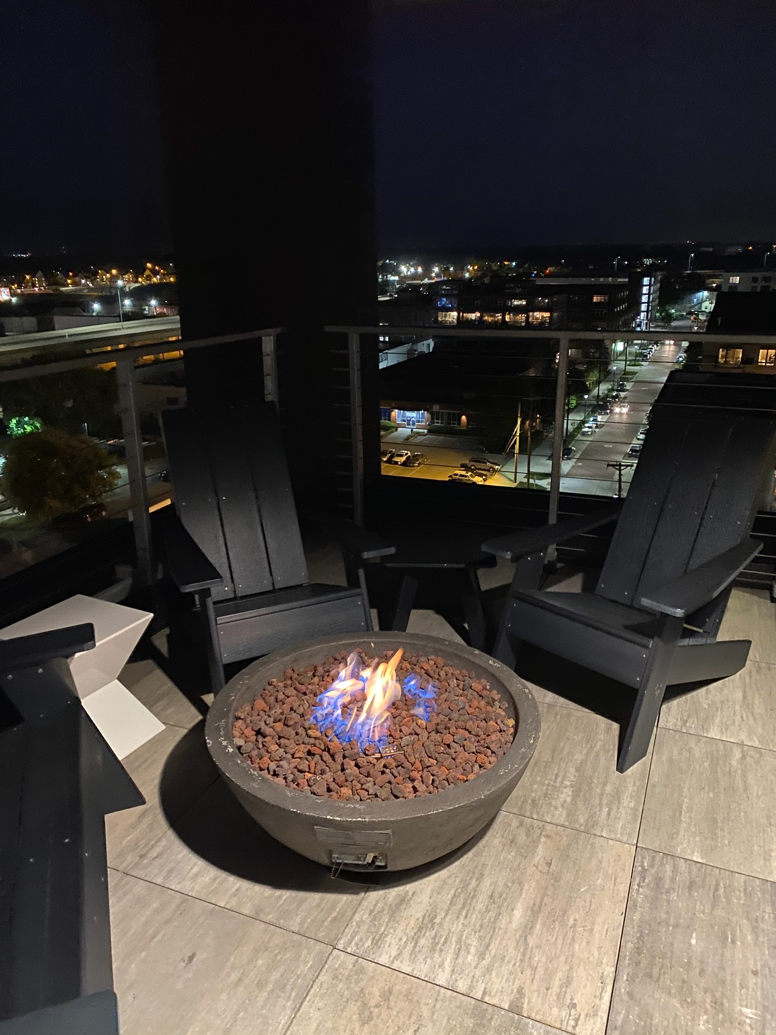 A stylish outdoor lounge area featuring a glowing fire pit and city views at night.