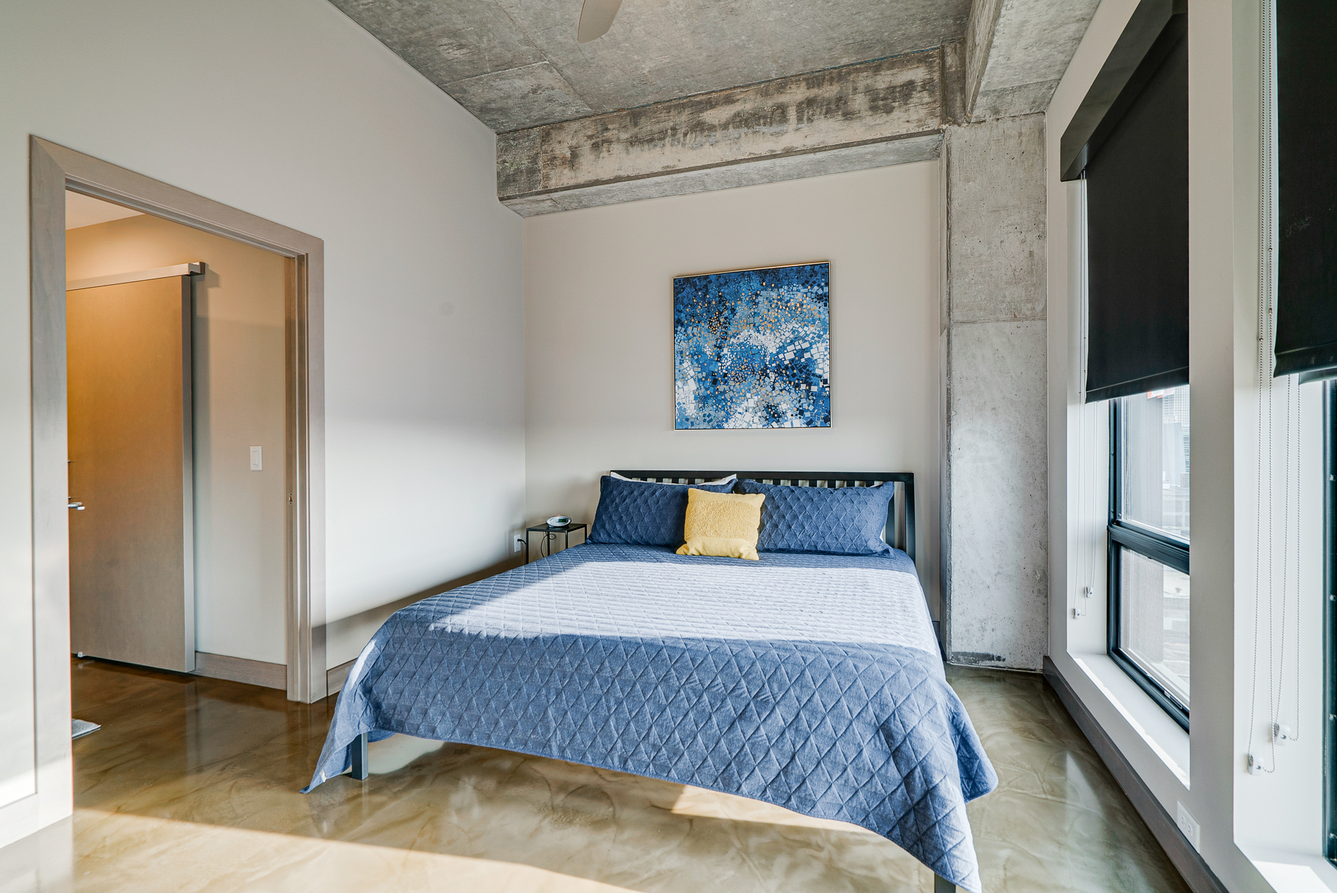 A modern and minimalist bedroom featuring a blue quilted bed and abstract wall art.