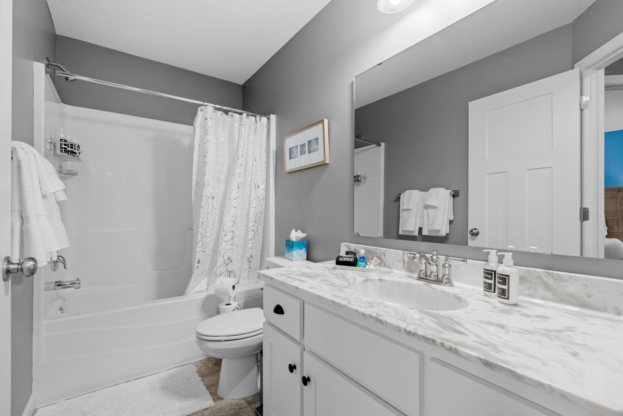A modern bathroom with a marble countertop and floral shower curtain.