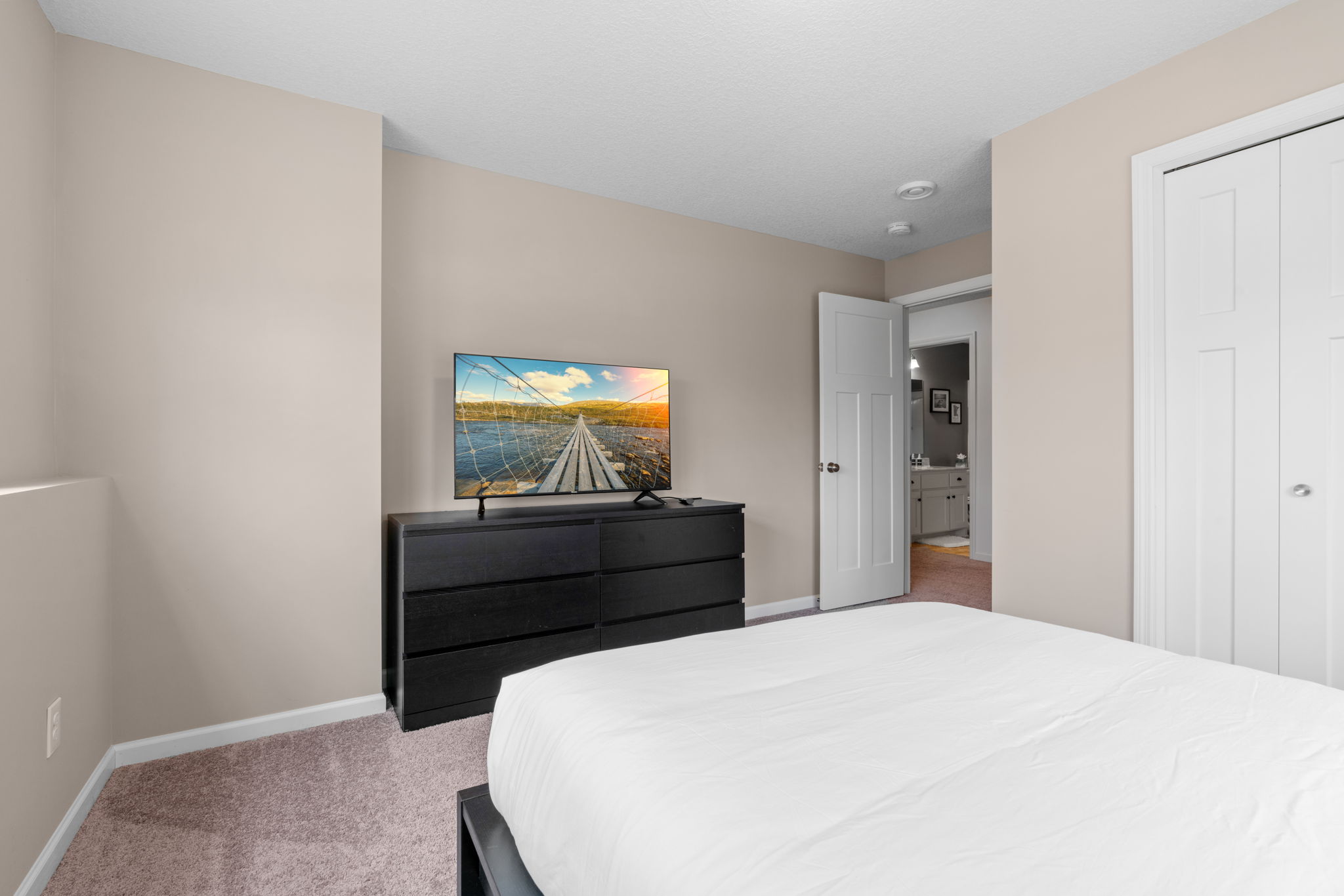 A cozy bedroom featuring a neatly made bed and a flat-screen TV displaying a scenic landscape.