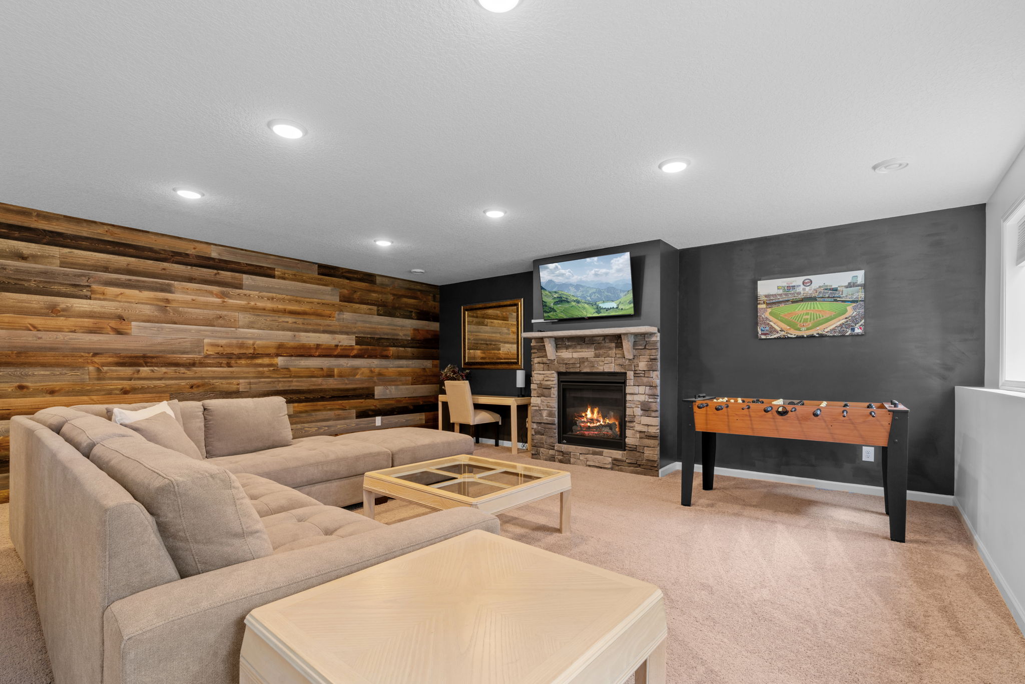 A cozy living area featuring a sectional sofa, stone fireplace, and foosball table.