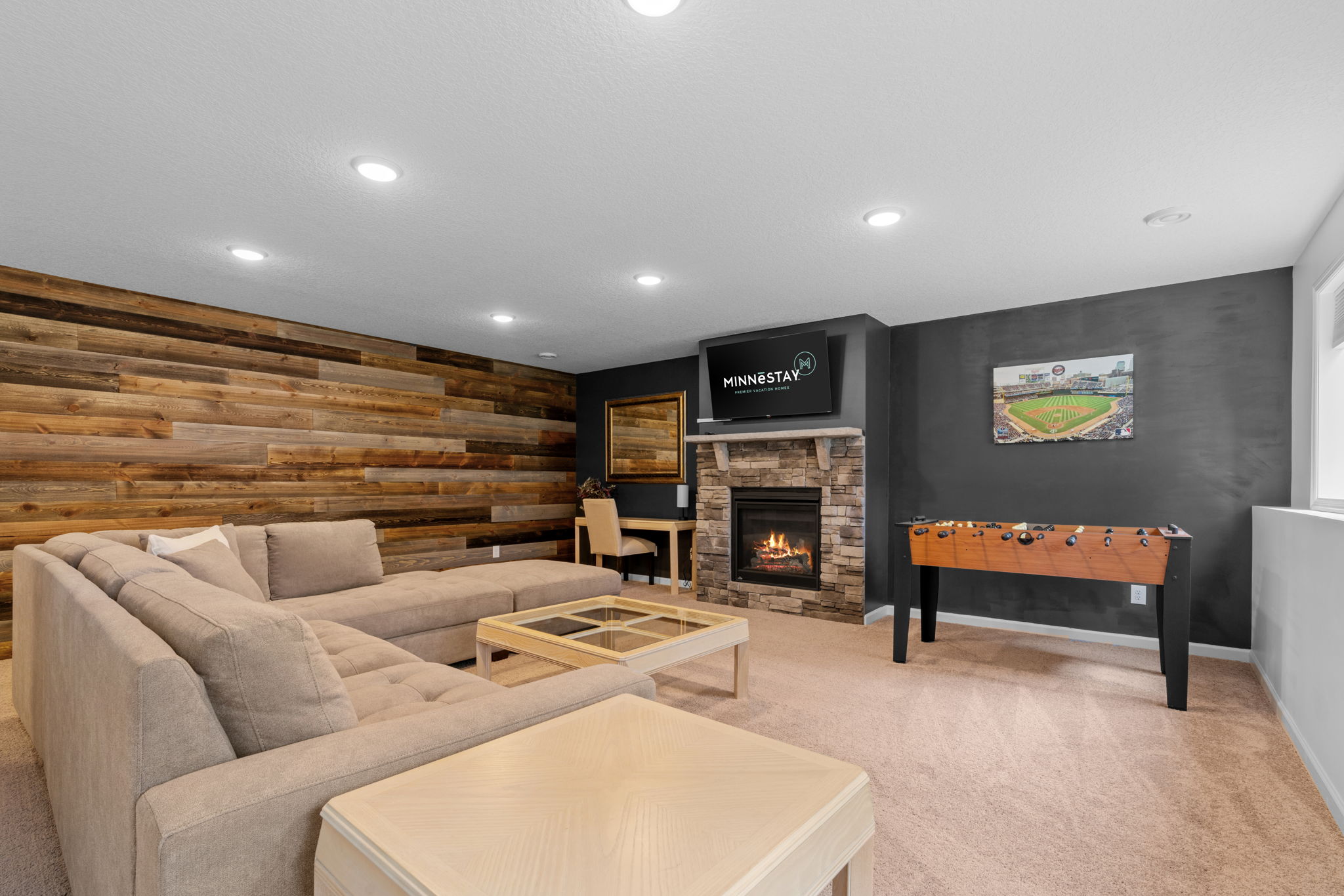 A cozy family room featuring a sectional sofa, stone fireplace, and foosball table.