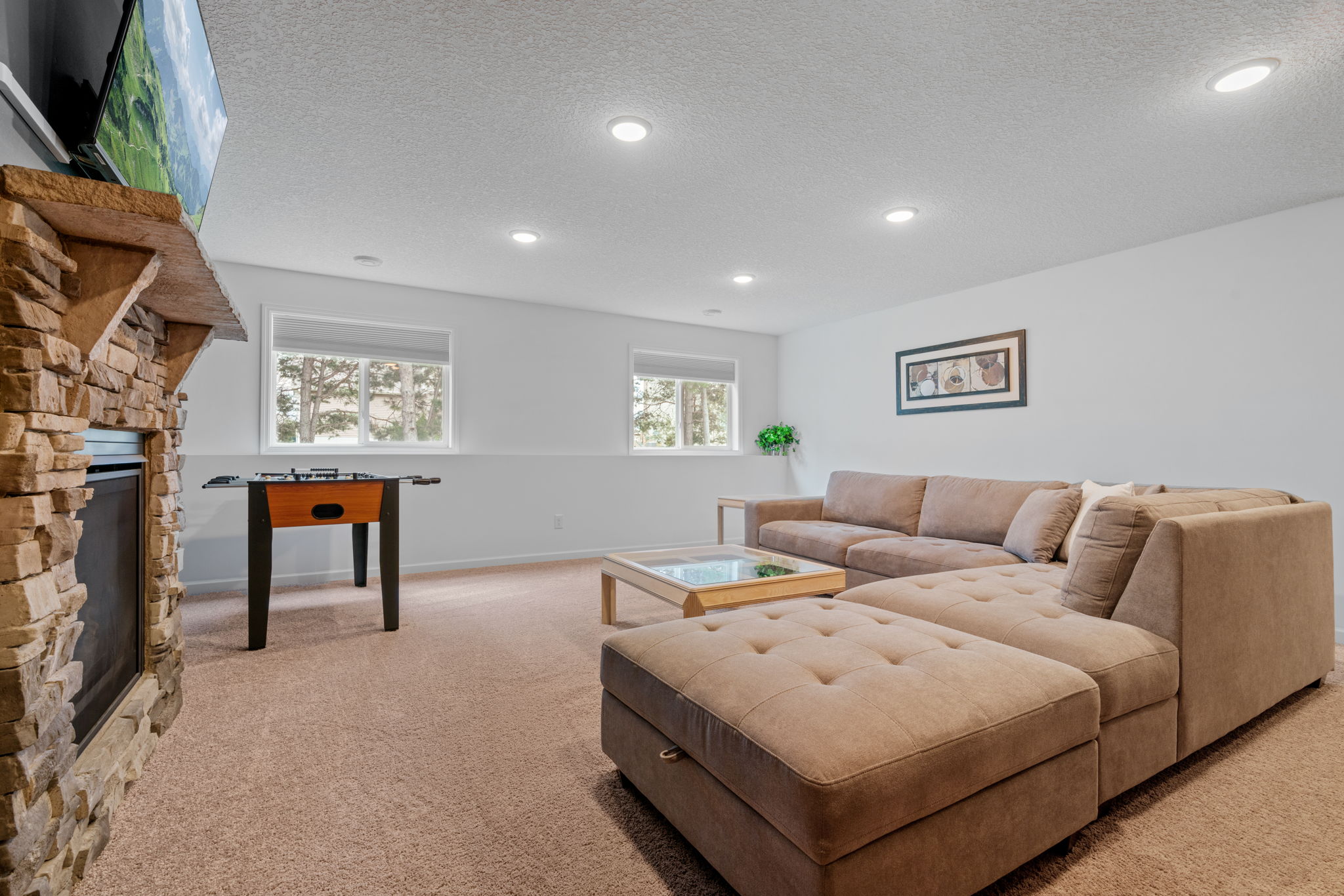 A cozy living room with modern decor, featuring a sectional sofa, foosball table, and a stone fireplace.
