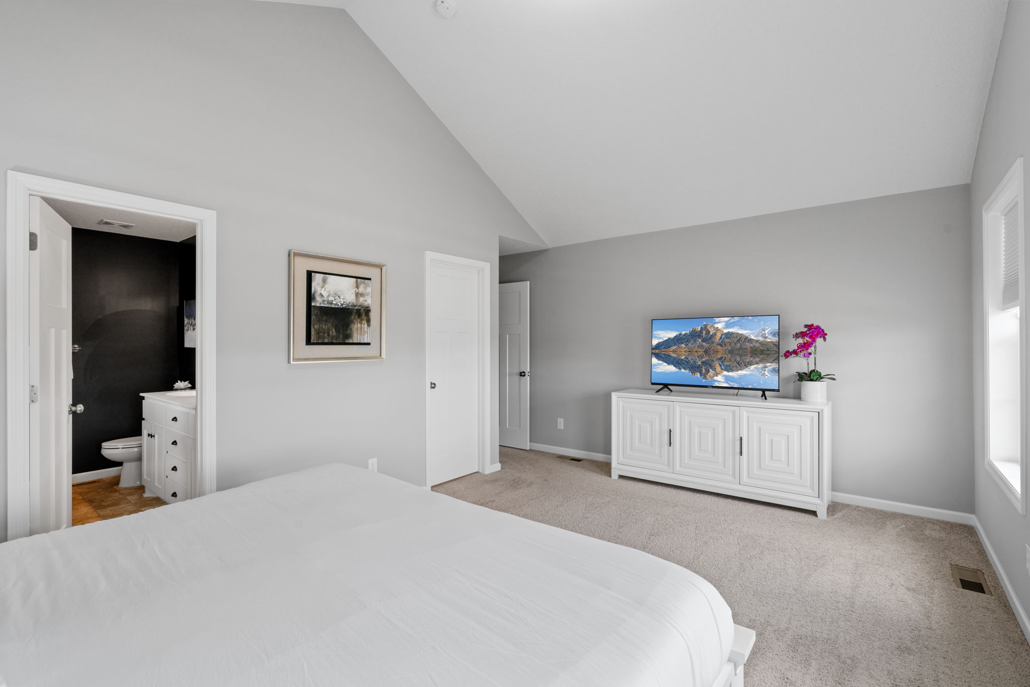 A modern bedroom featuring a high ceiling, white furnishings, and a stylish TV with a scenic view.