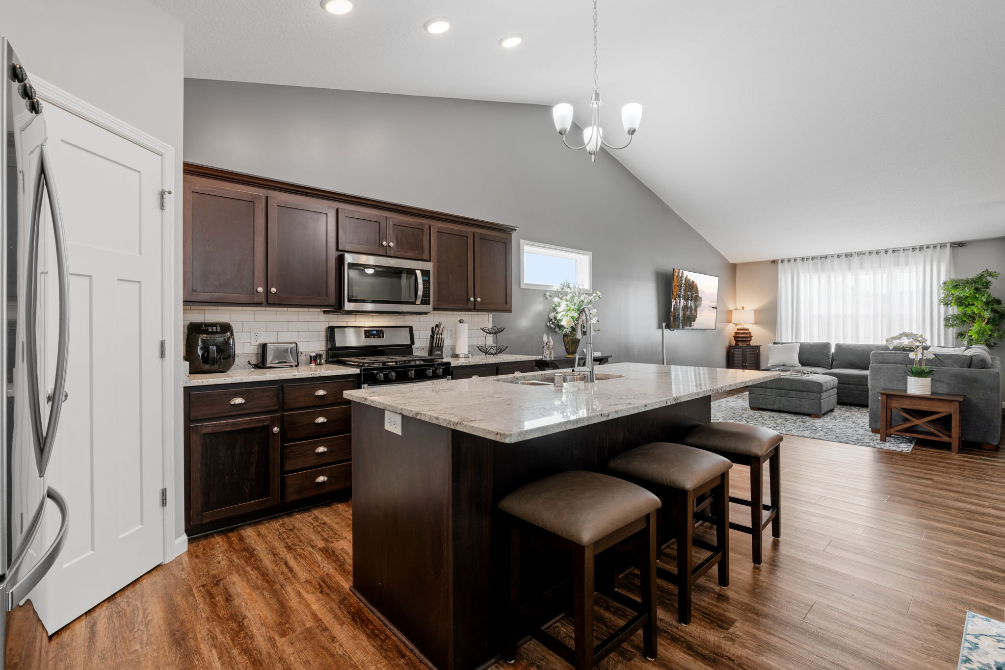 A modern kitchen seamlessly flows into a cozy living area, characterized by dark wood elements and a warm color palette.