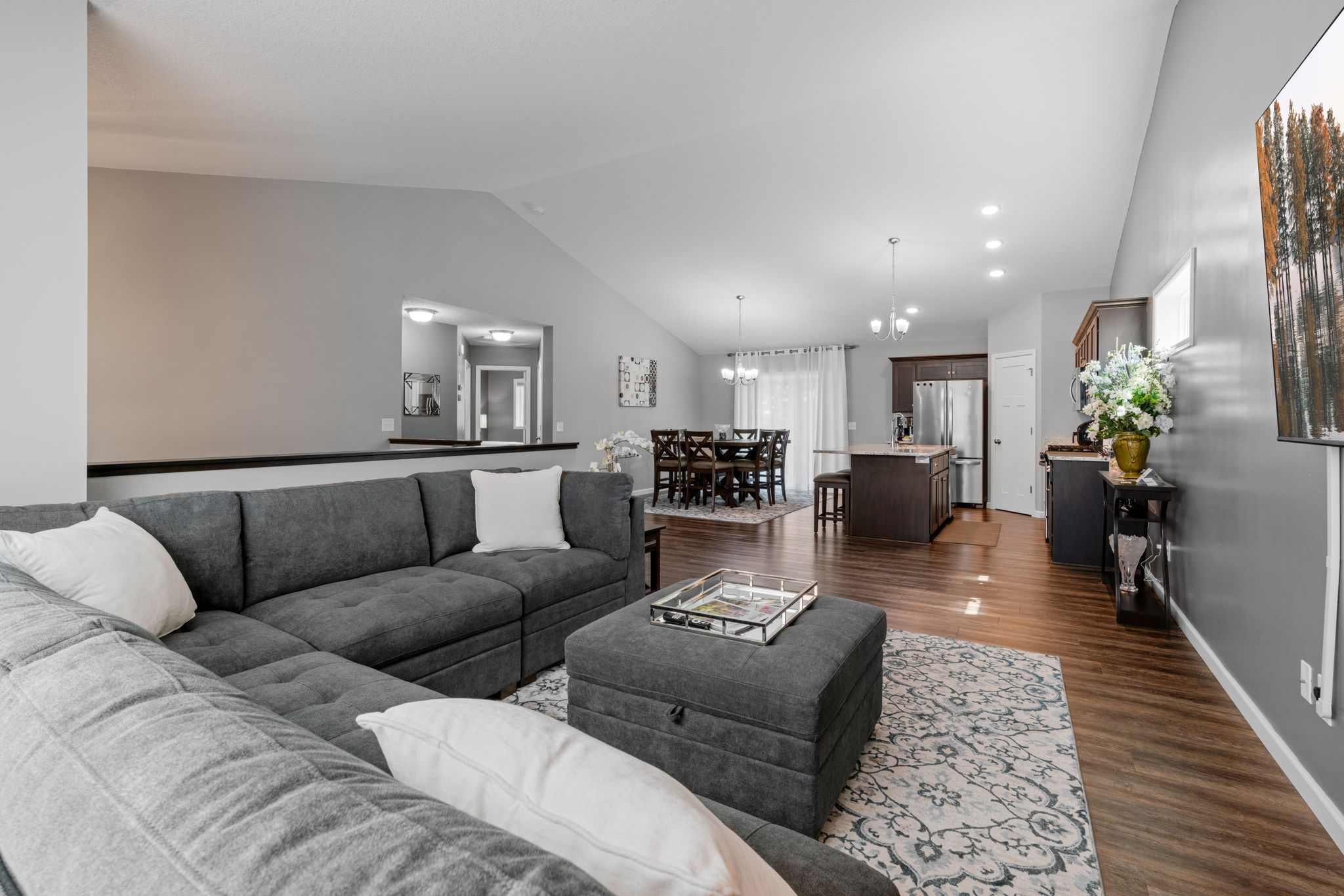 A cozy and modern open-concept living area featuring a gray sectional sofa and sleek dining space.