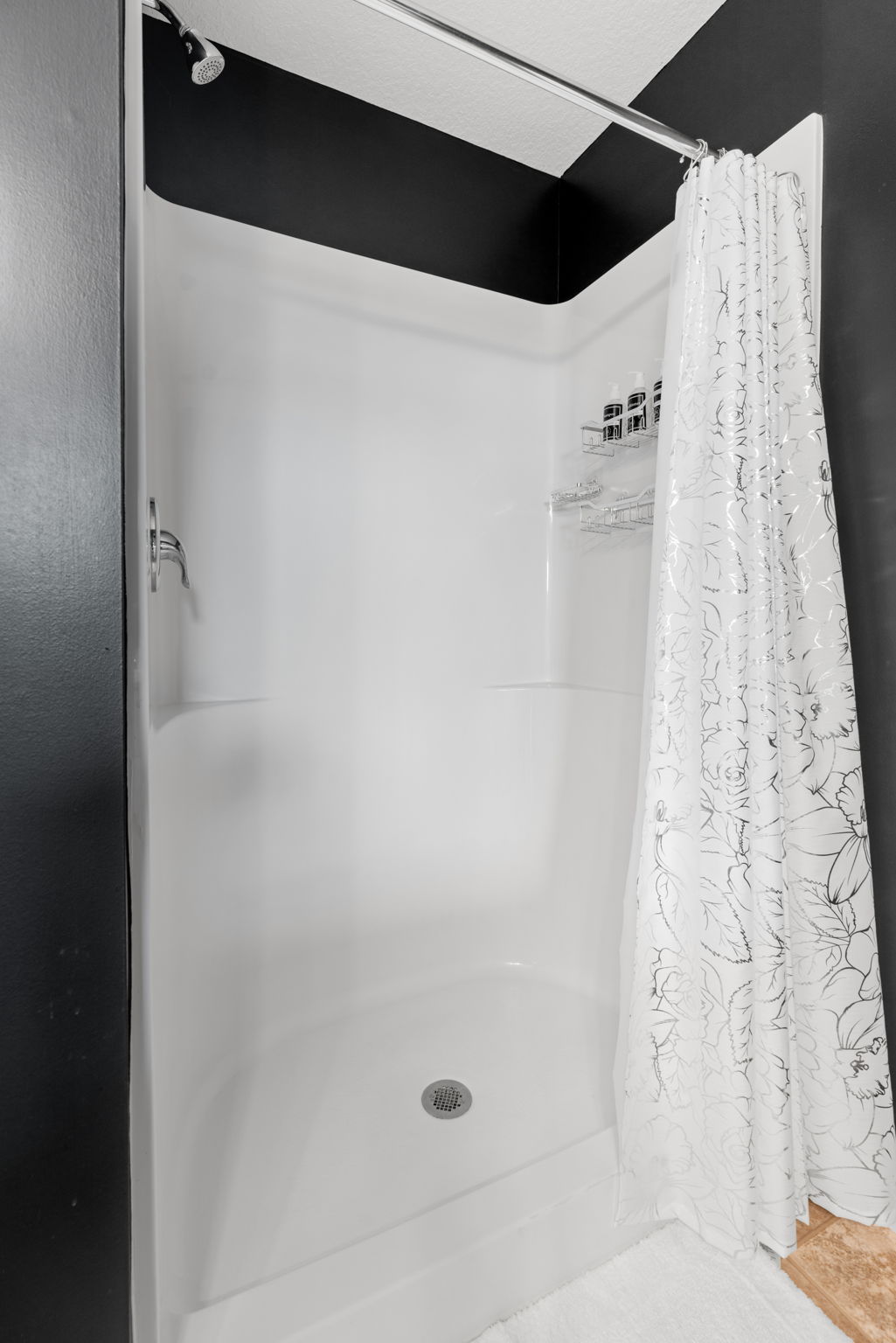 A modern shower stall with a minimalist design featuring a floral curtain and black walls.