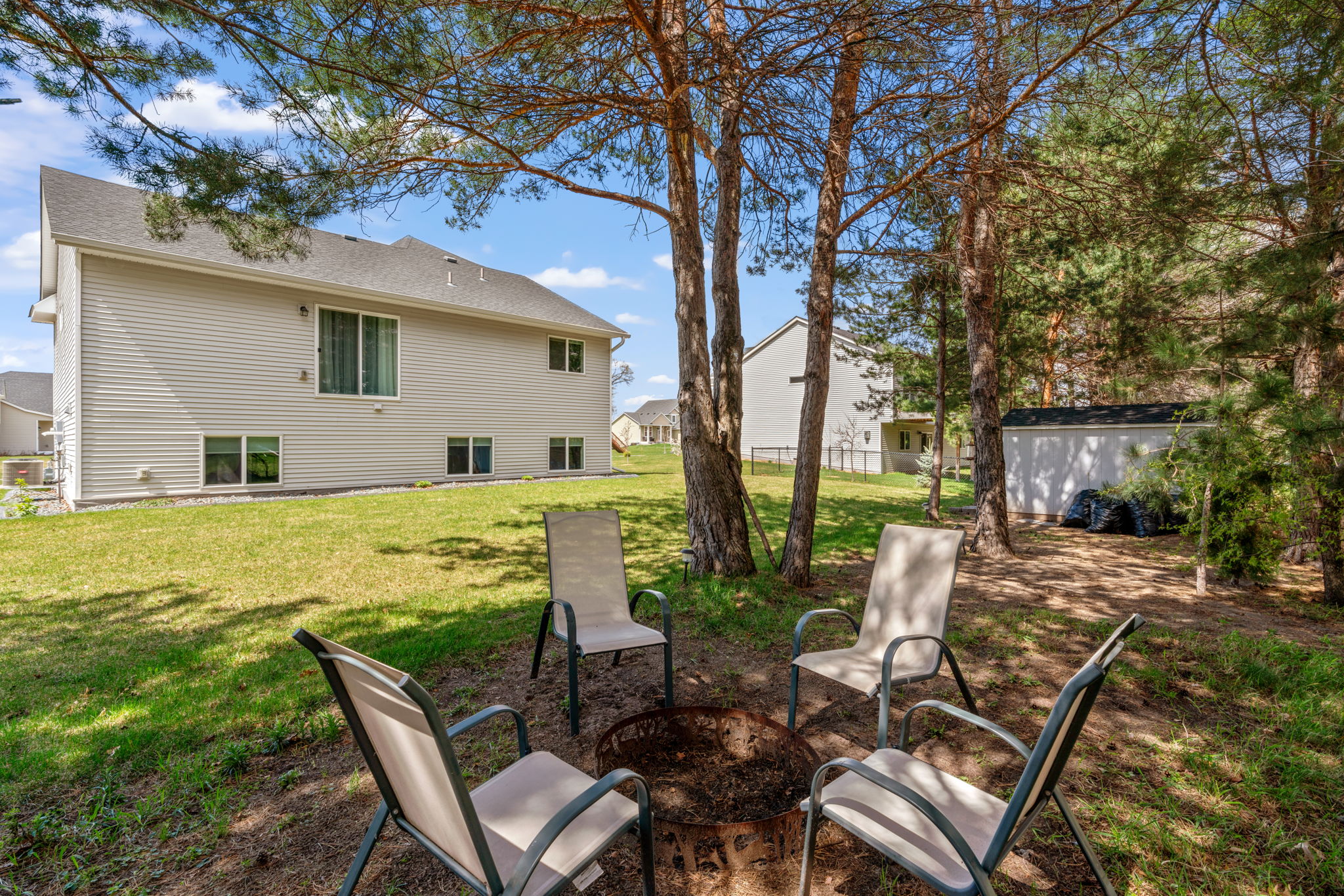 A cozy backyard fire pit area surrounded by trees and modern homes.