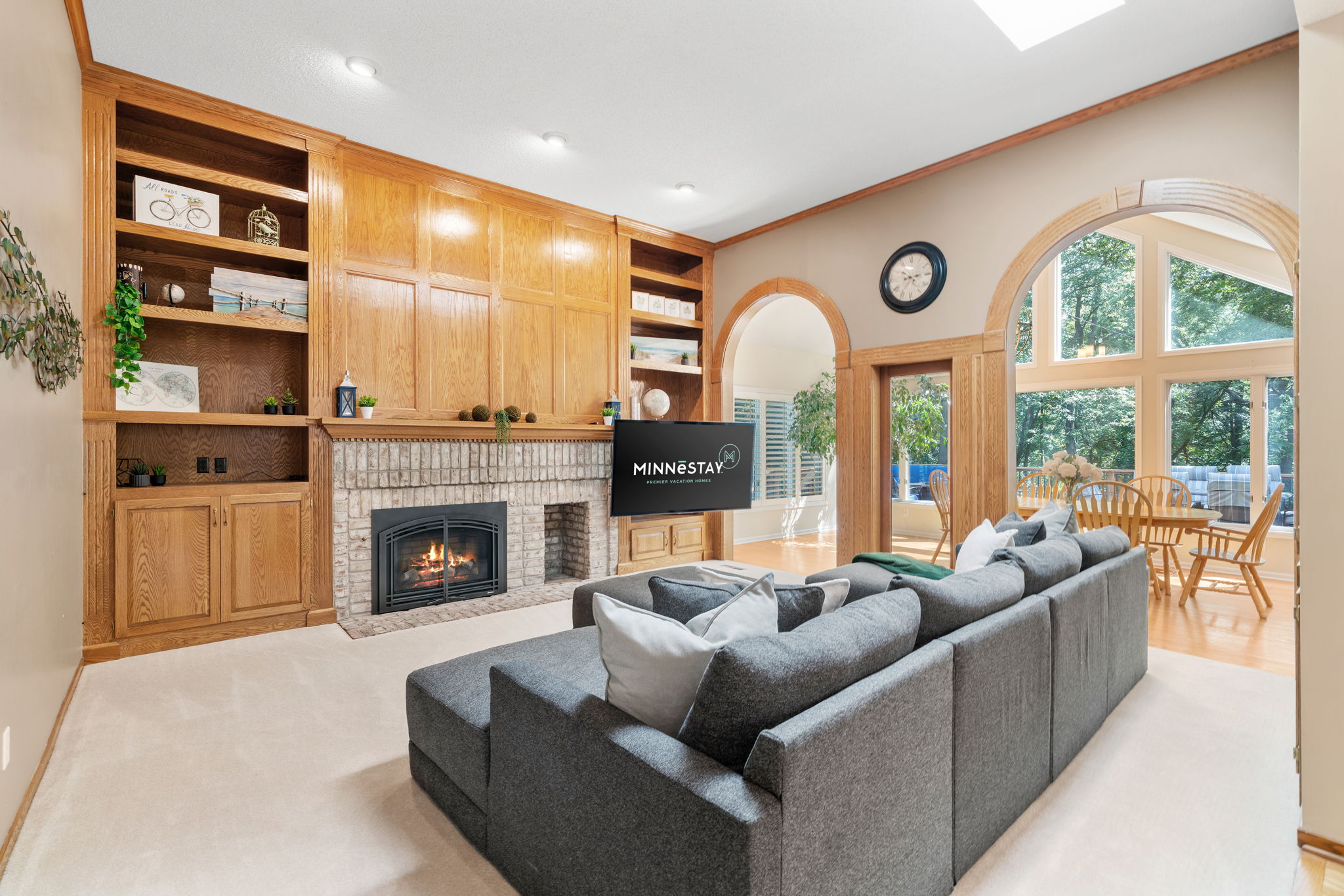 Inviting living room featuring gray sectional sofa, brick fireplace, and wooden shelving.