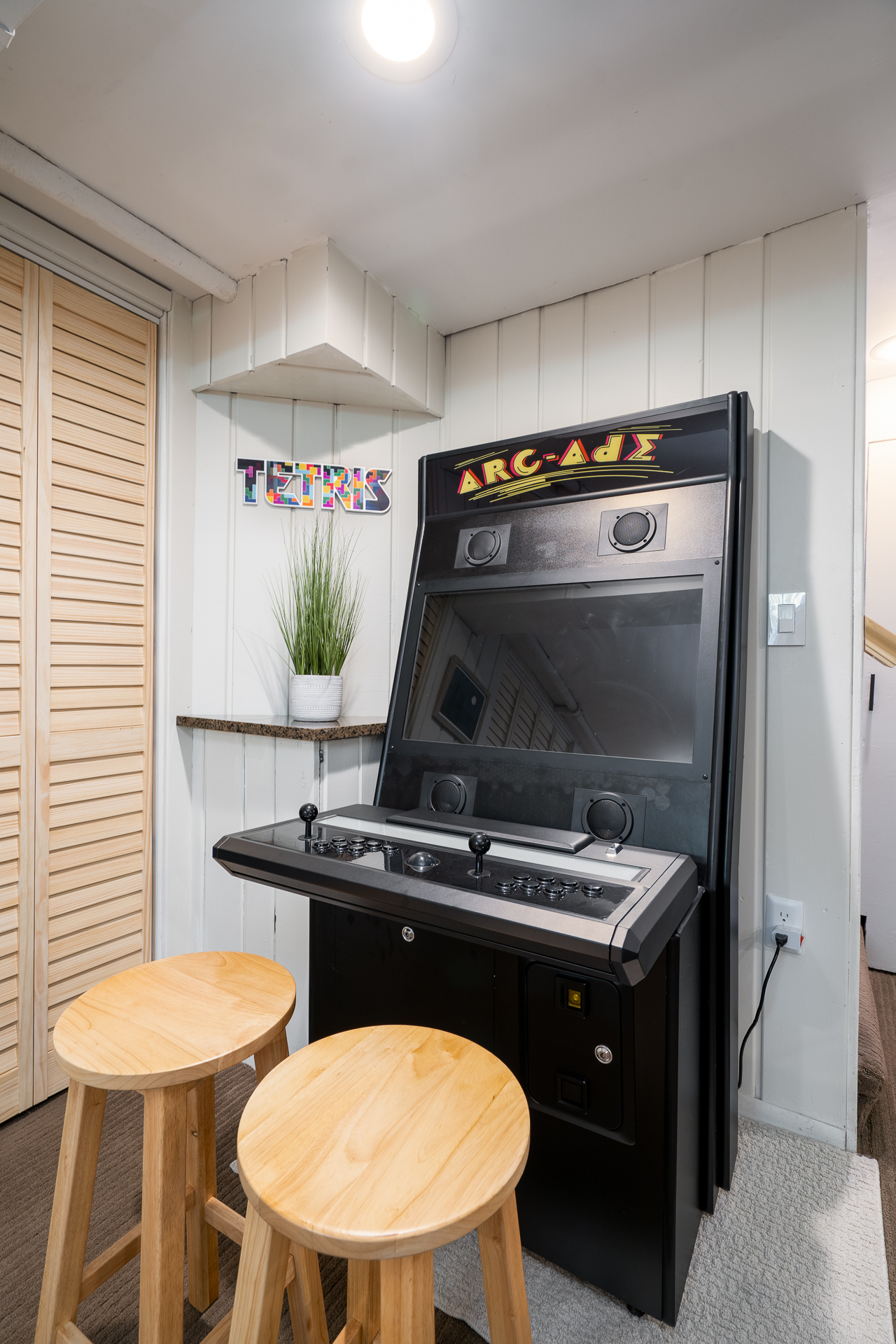 A stylish corner featuring an "ARC-ade" arcade machine with stools and decorative elements.
