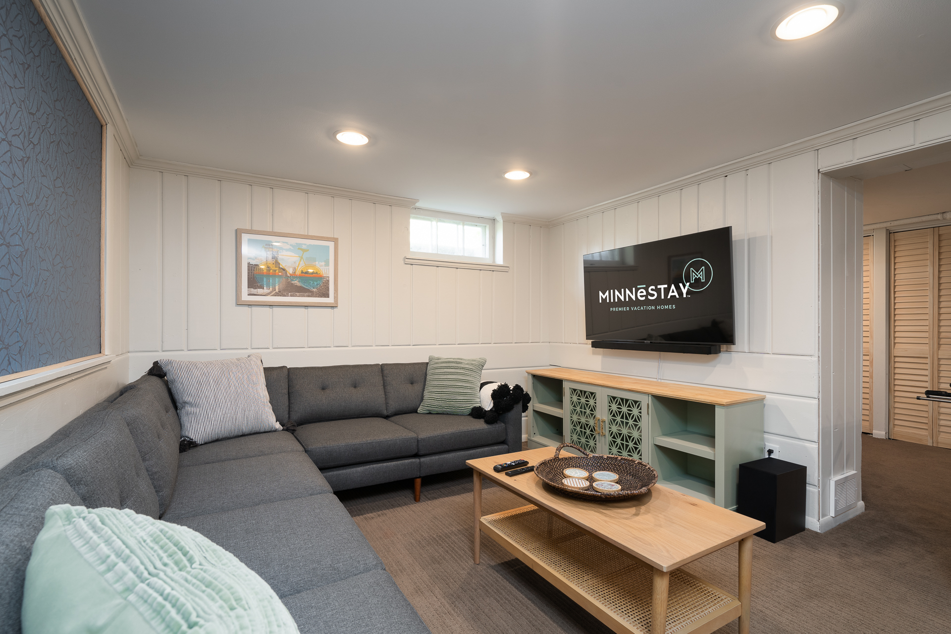 A cozy living room featuring a modern gray sectional sofa and a TV with the 'Minnestay' logo.